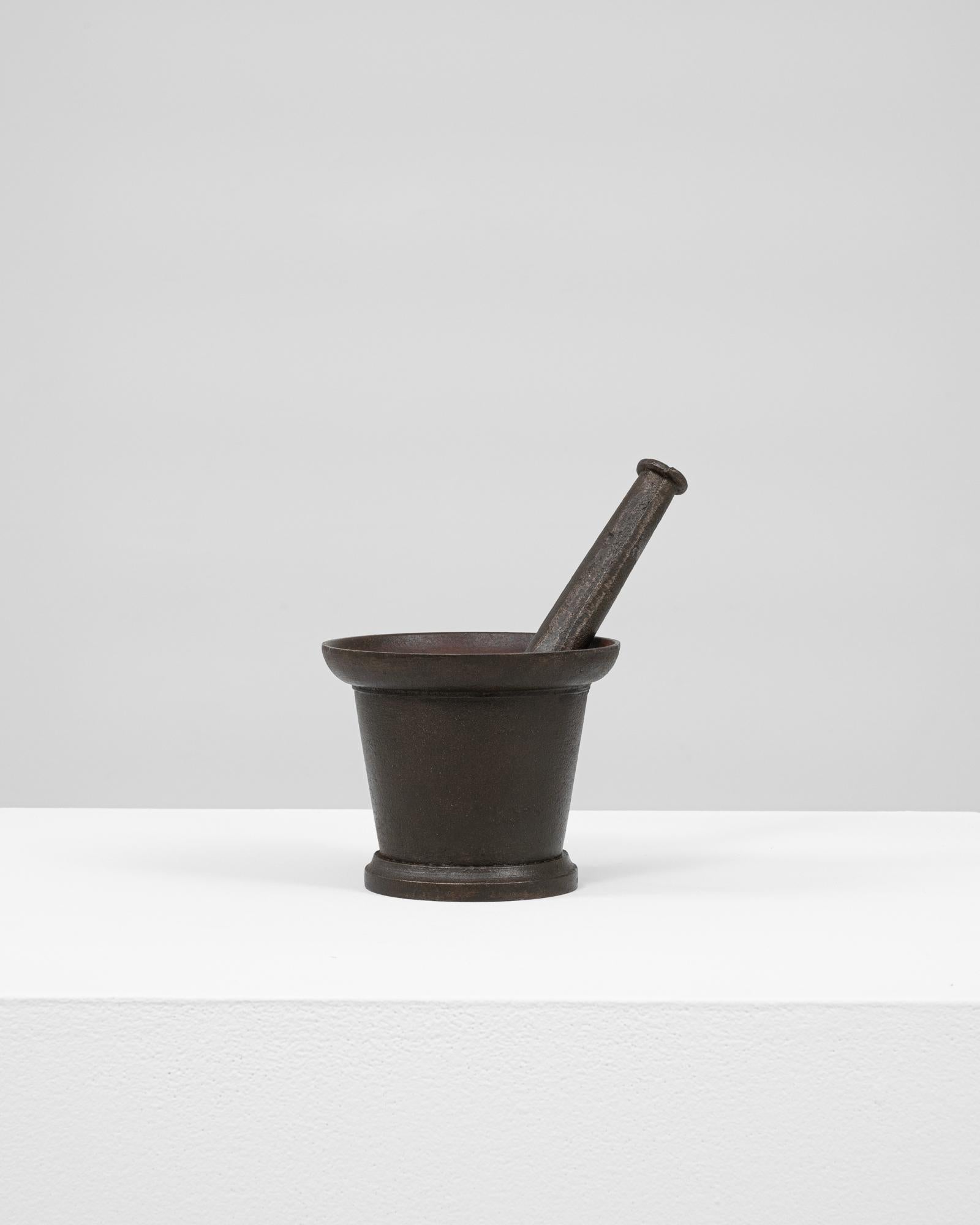 This 19th Century French cast iron mortar with pestle is a compelling relic of traditional apothecary and culinary practices. Cast in a classic tapered form, the mortar features a wide flared rim and sturdy base, providing both functionality and