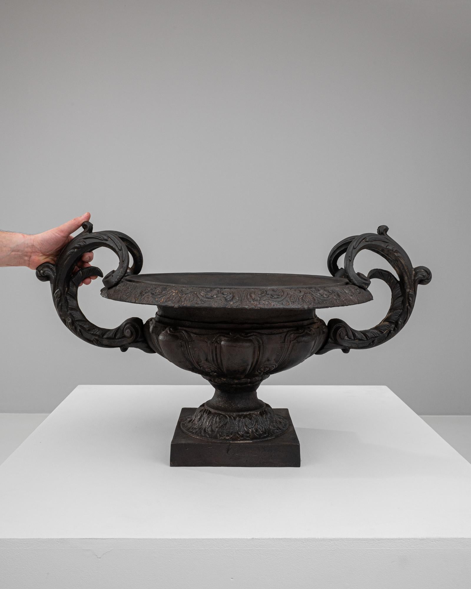 This 19th Century French Cast Iron Planter is a masterpiece of decorative art, infusing aristocratic elegance into any space it graces. Ornately carved with intricate patterns, the bowl of the planter sits majestically atop a fluted pedestal. It's