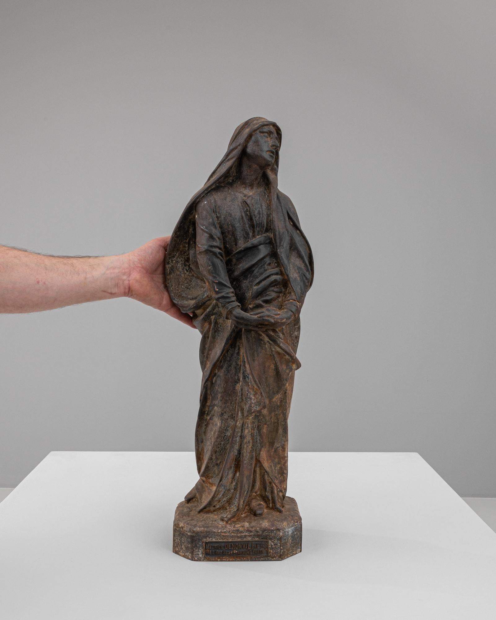 This evocative 19th Century French Cast Iron Sculpture captures the profound emotion and exquisite detail synonymous with the era's artistry. The figure, robed in beautifully sculpted garments that flow with lifelike grace, carries a contemplative