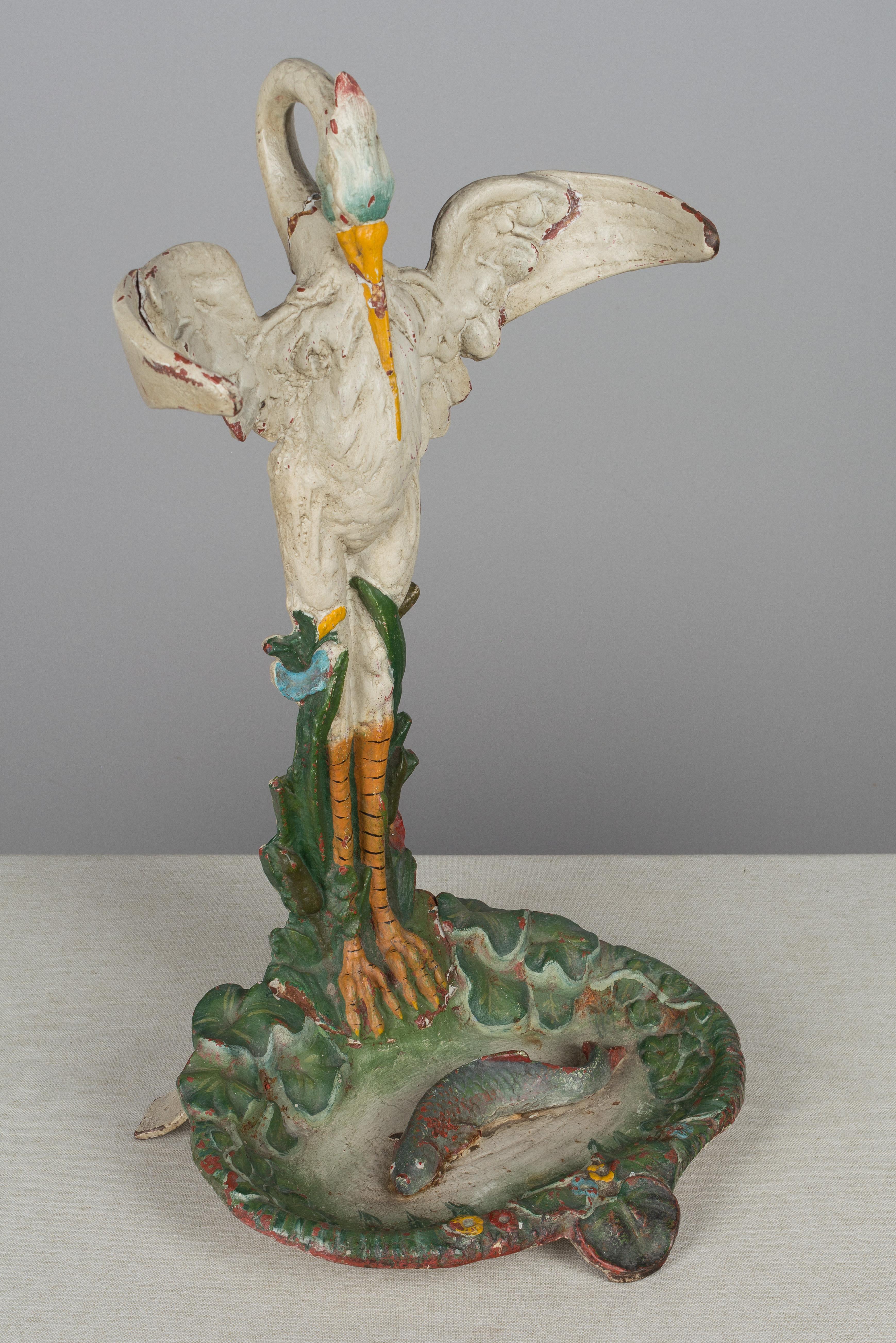 A whimsical 19th century French cast iron polychrome painted umbrella stand. Beautifully detailed sculpture of a crane standing at the water's edge, eyeing a fish in the pond below. The bird's outstretched wings curve to hold the umbrellas upright