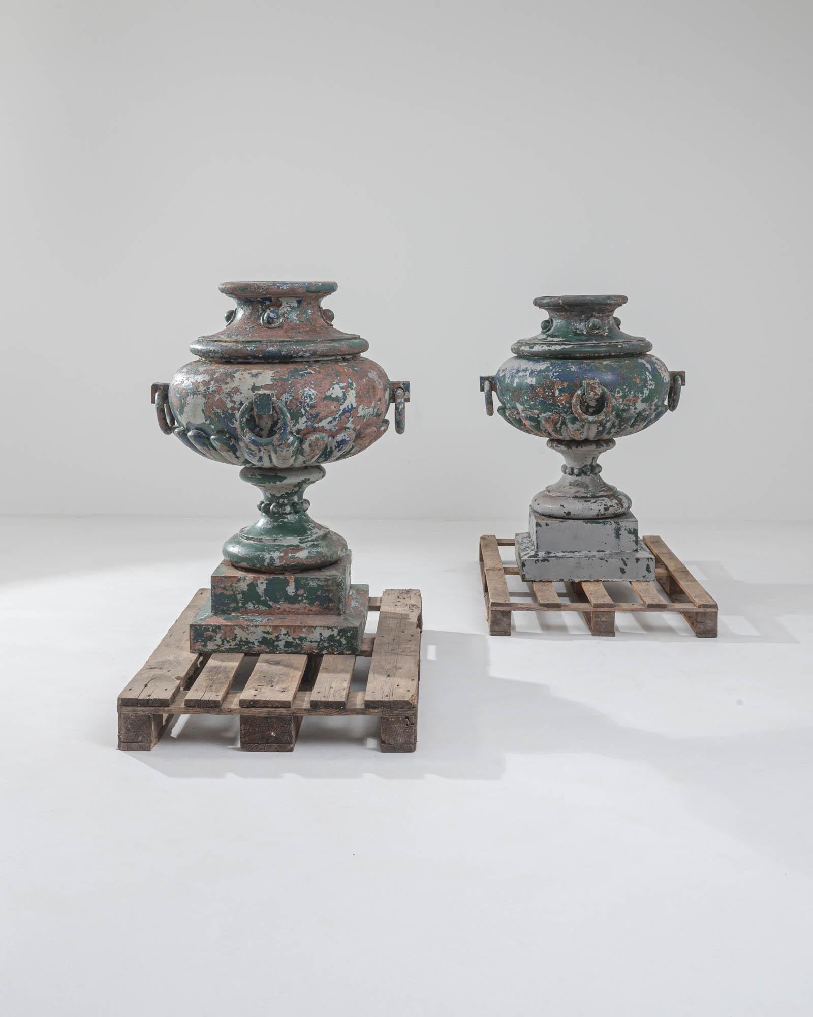 This rare pair of antique cast iron vessels combine a distinctive patina with a striking silhouette. Made in France in the 1800s, these pieces were likely used as planters or garden accents. The ornamental form plays astutely with volume: a slender