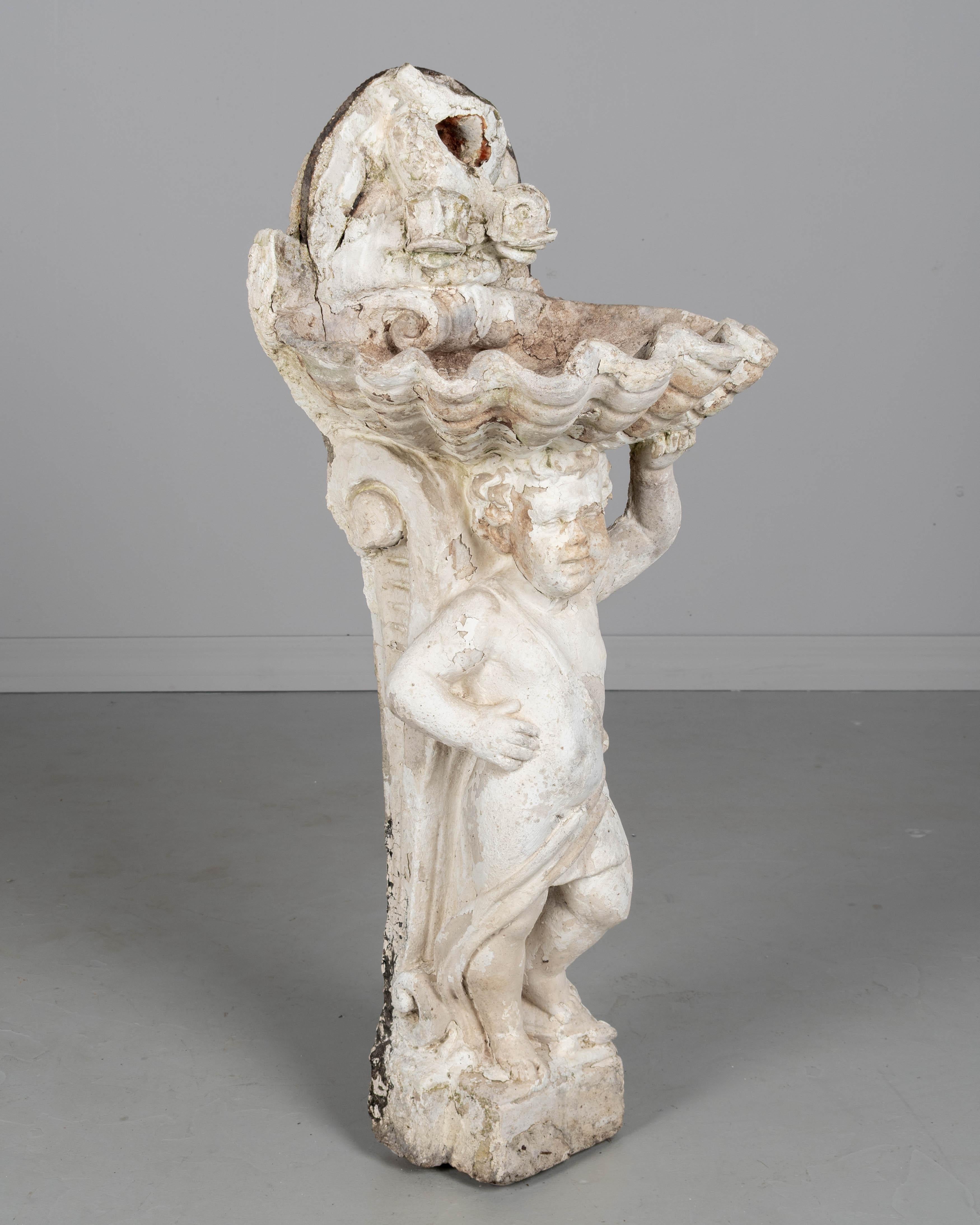 Fontana in pietra fusa in stile neoclassico francese del XIX secolo. Un bacino a forma di conchiglia con un paio di beccucci a forma di delfino è tenuto in alto da un cherubino, o putto, con il piede appoggiato su una tartaruga. Patina rovinata