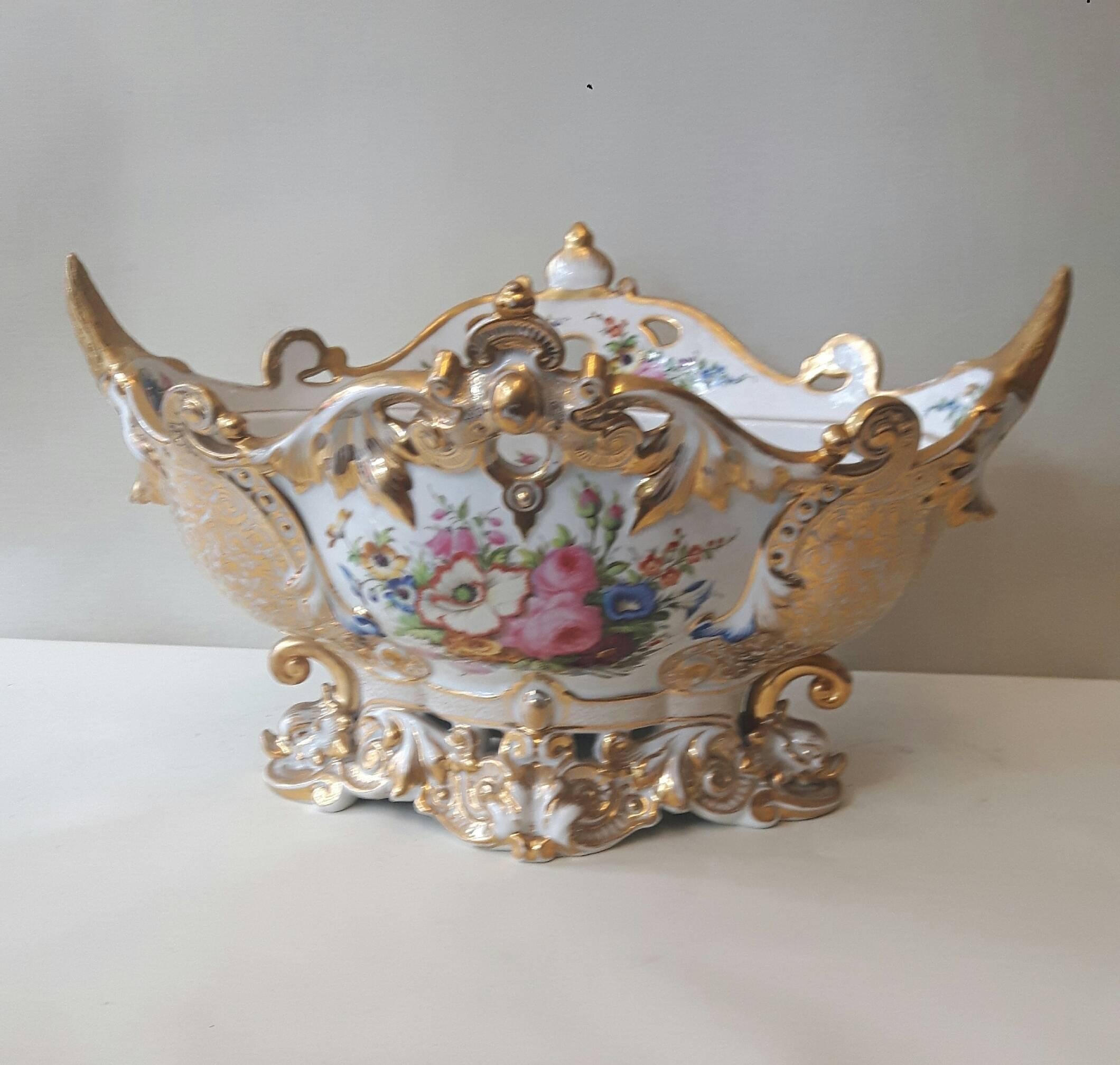 An elegant 19th century Paris porcelain centrepiece, the hand-decorated bowl resting on four gilded dolphin heads with curled tails. The rococo shaped rim is adorned with gilded swan heads and armorial swags. The inside of the centrepiece is loosely