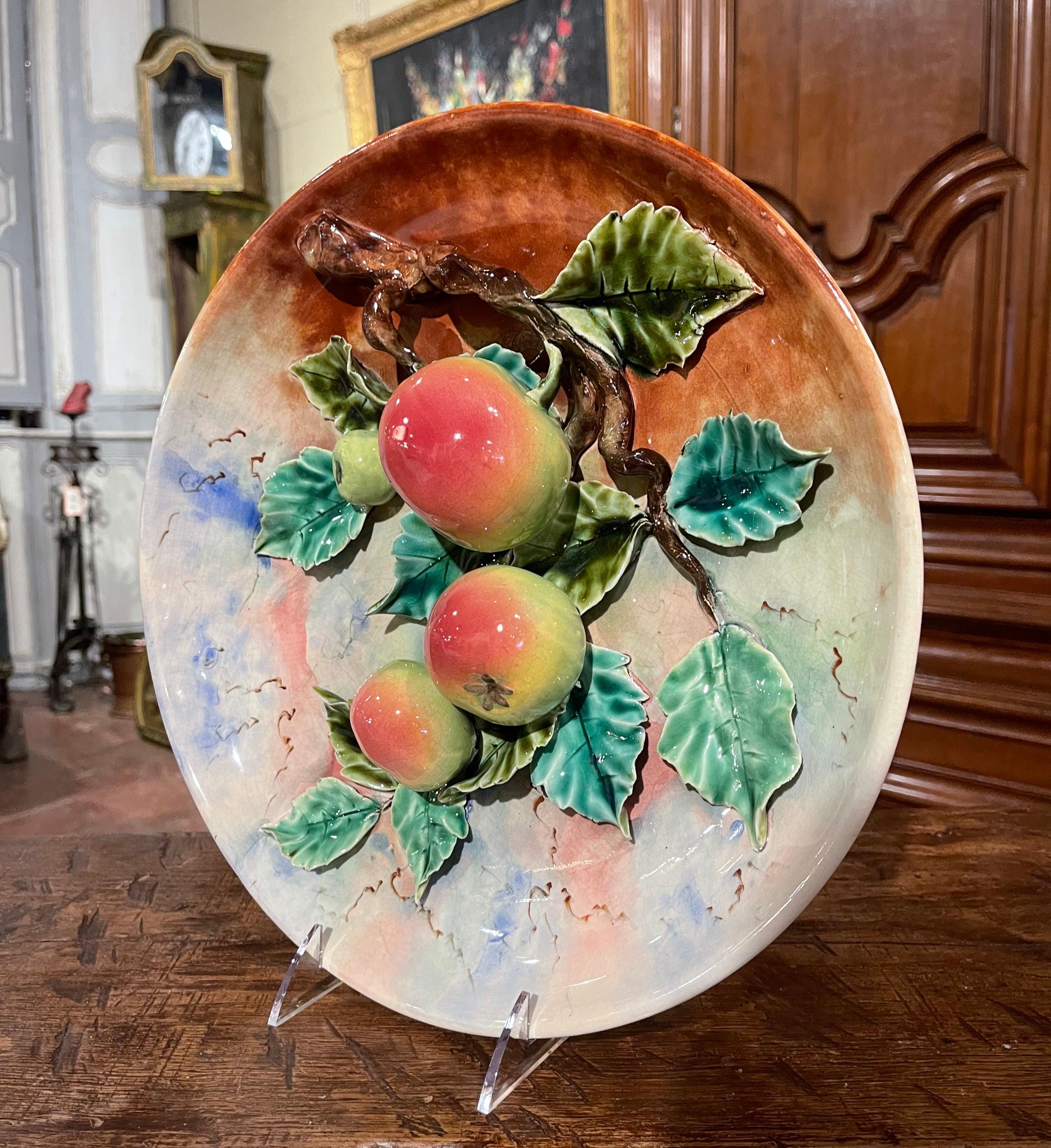 Cette assiette à fruits antique et colorée en majolique a été sculptée en France, vers 1890. Le grand plateau circulaire présente quatre pommes vertes et rouges peintes à la main et suspendues à une branche d'arbre couverte de feuilles vertes. Les