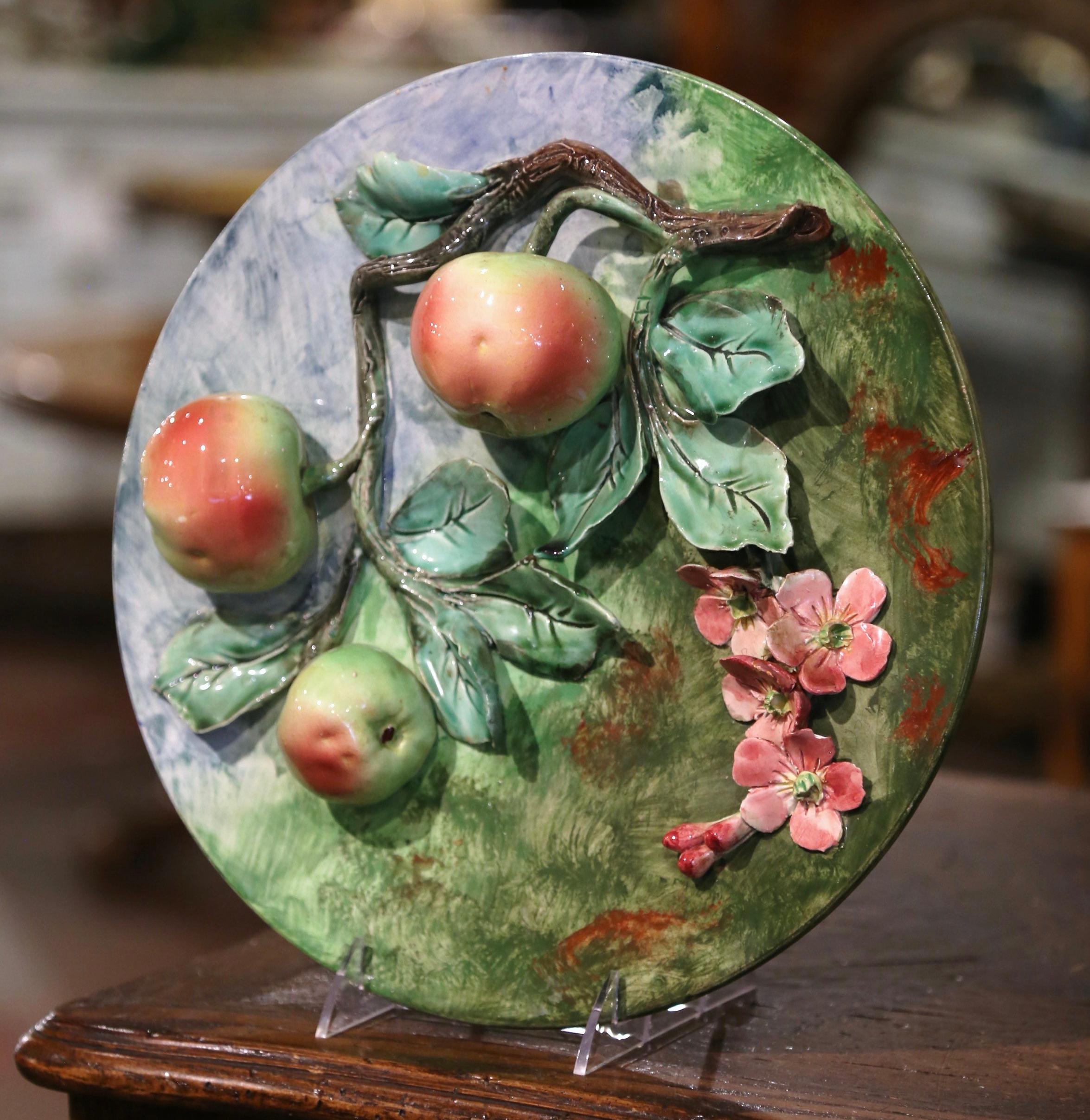 This colorful, antique Majolica plate was sculpted in France, circa 1880. The large, round, hand painted platter features pink flowers and three red and yellow apples hanging from a tree branch covered with green leaves. The sculpted additions are