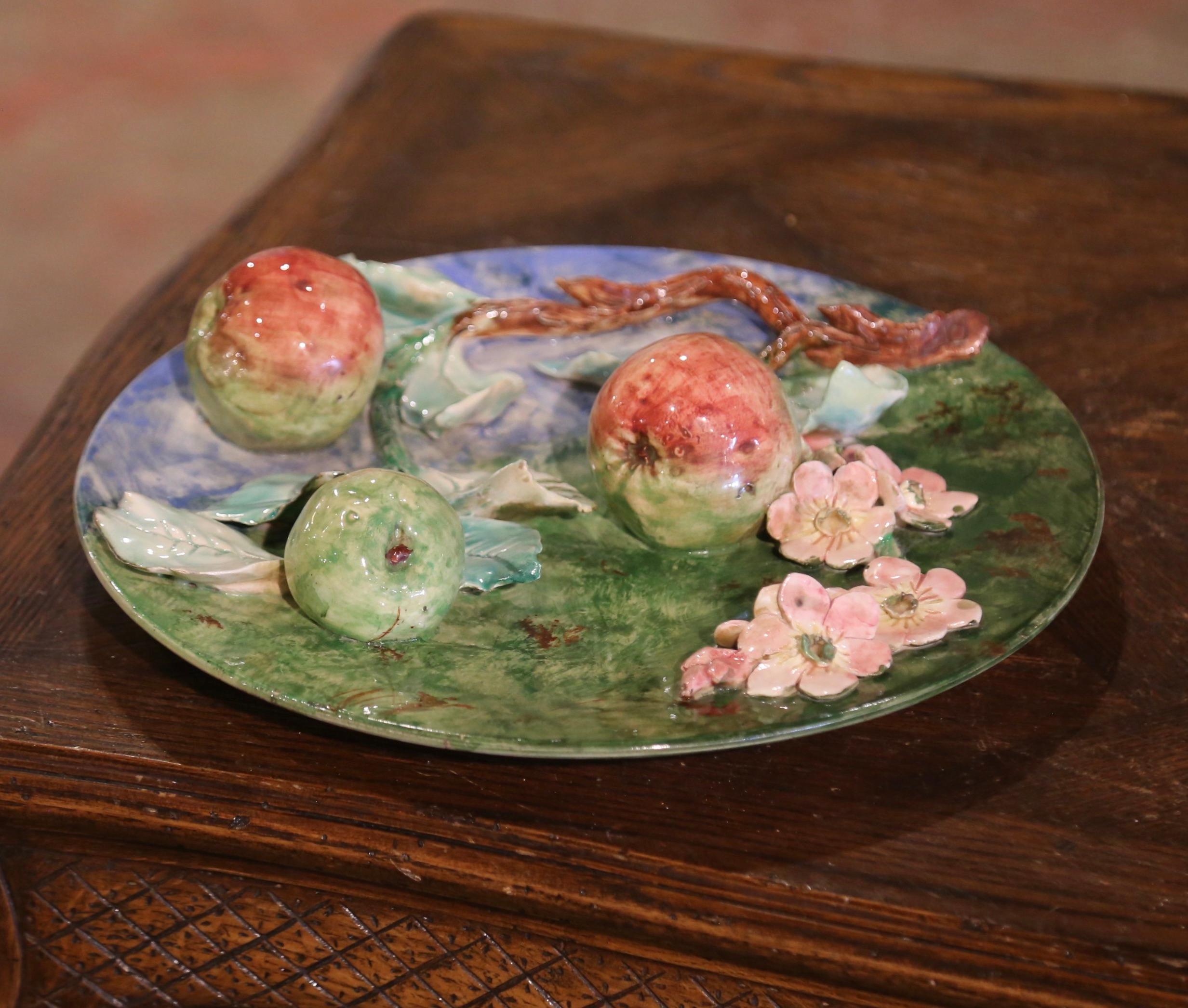 Decora una parete della cucina con questo coloratissimo piatto antico in maiolica! Scolpito in Francia, intorno al 1880, il grande piatto da portata è  Di forma rotonda, presenta motivi dipinti a mano con tre mele rosse e gialle appese a un ramo