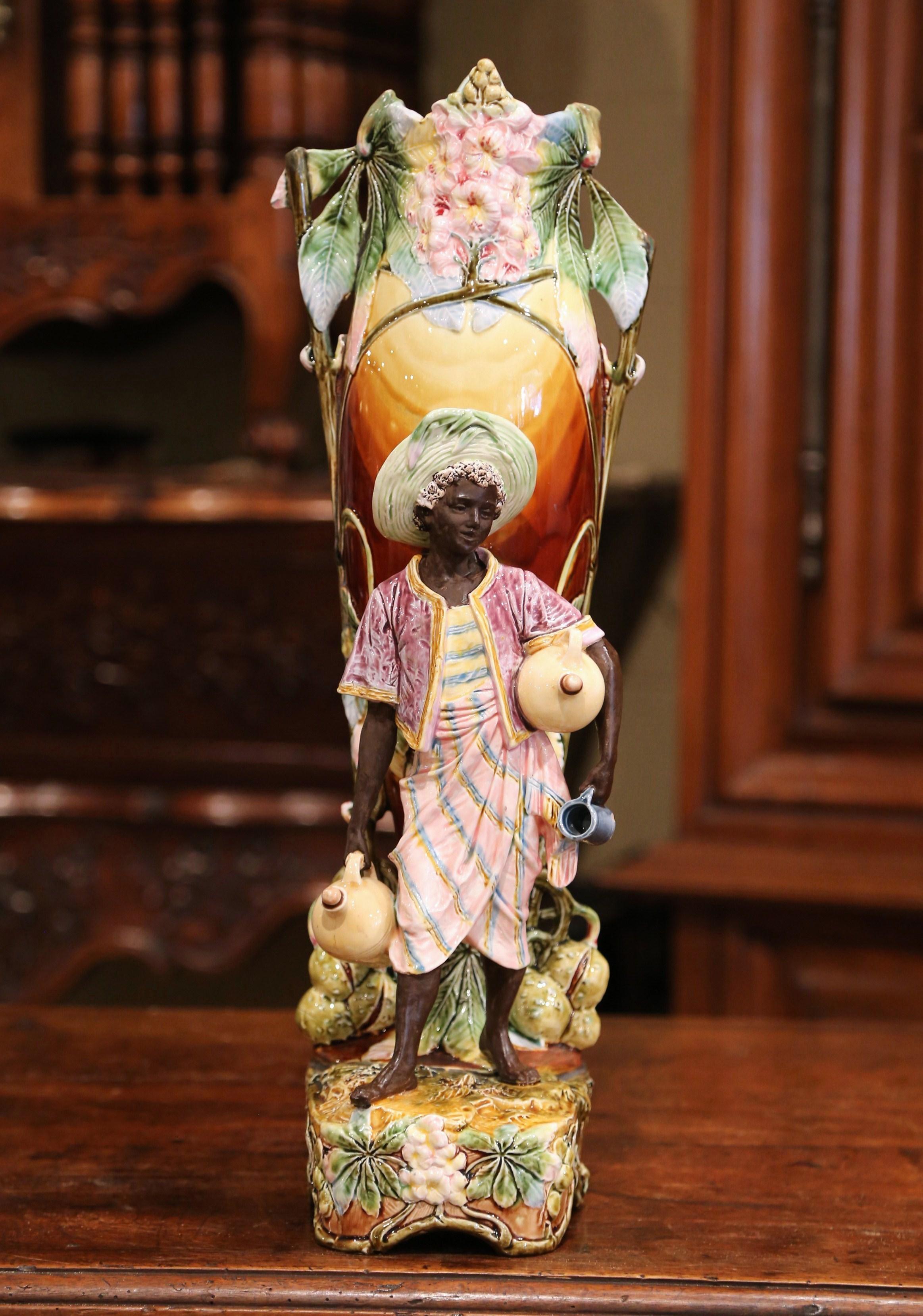 Place this tall, hand painted Majolica vase on a console or a shelf. Crafted in France circa 1880, the colorful ceramic vase features a boy sculpture holding water jars. A large, urn-shaped vase is at the core of the piece, and is embellished with