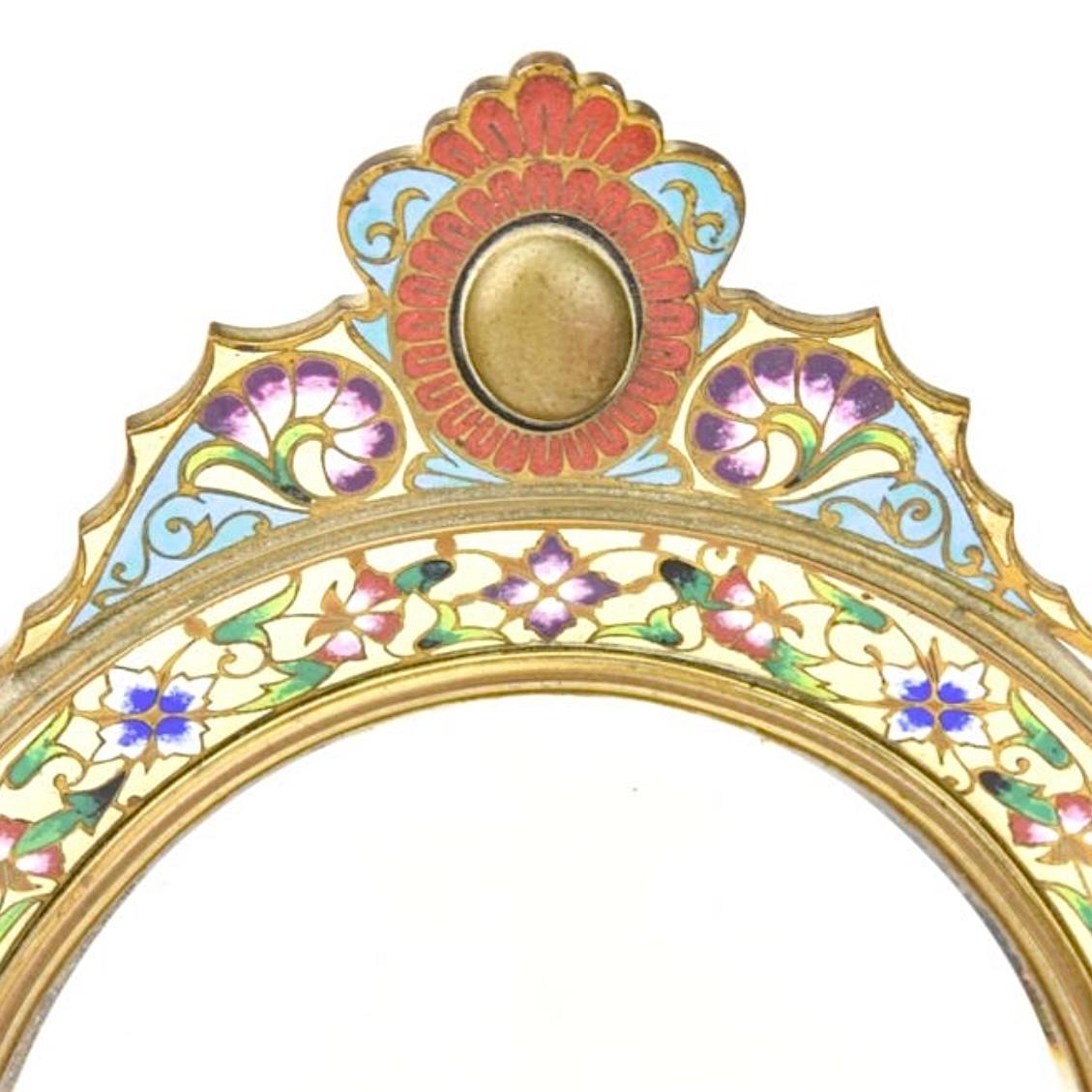 Our beautiful antique (late 19th century) mirror finely crafted from bronze with champleve enamel designs and beveled glass measures 18 inches tall and is in very good condition.  Decorated with leafy scrolls and floral garlands in gold, red, rust,