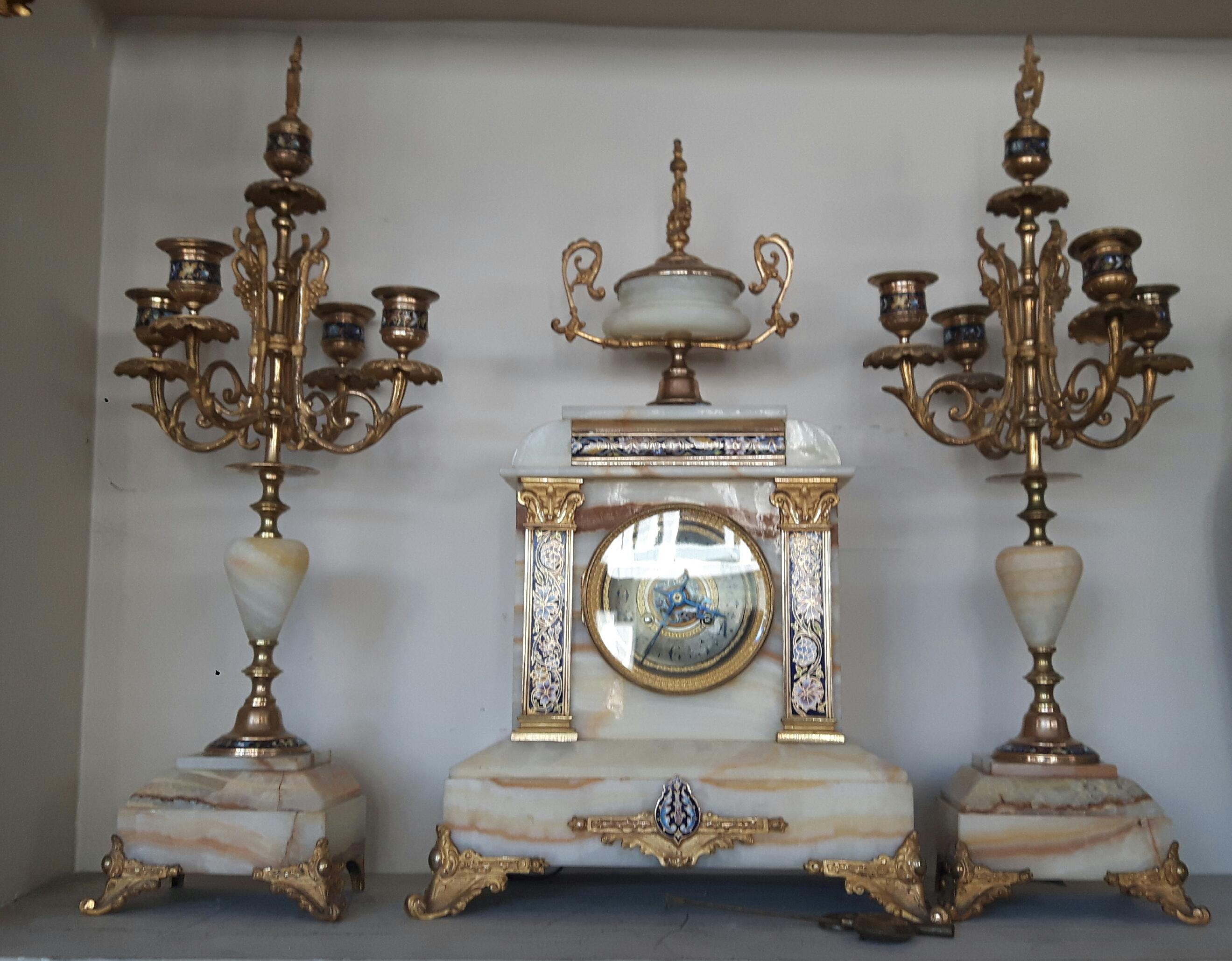 Three-piece marble and bronze Champlevé enamel clock garniture set, comprising of a central clock and a pair of candelabra. The clock is set on a white marble base on a rectangular plan.