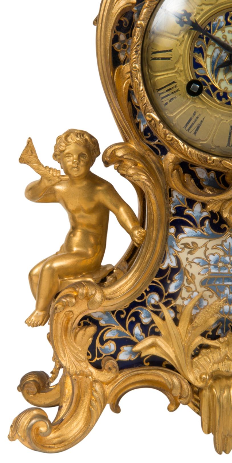 A very good quality 19th century French champlevé enamel and gilded ormolu clock garniture, each candelabra having five branches, enamel decoration and scrolling feet. The clock with an urn finial and swags either side, an eight day duration which