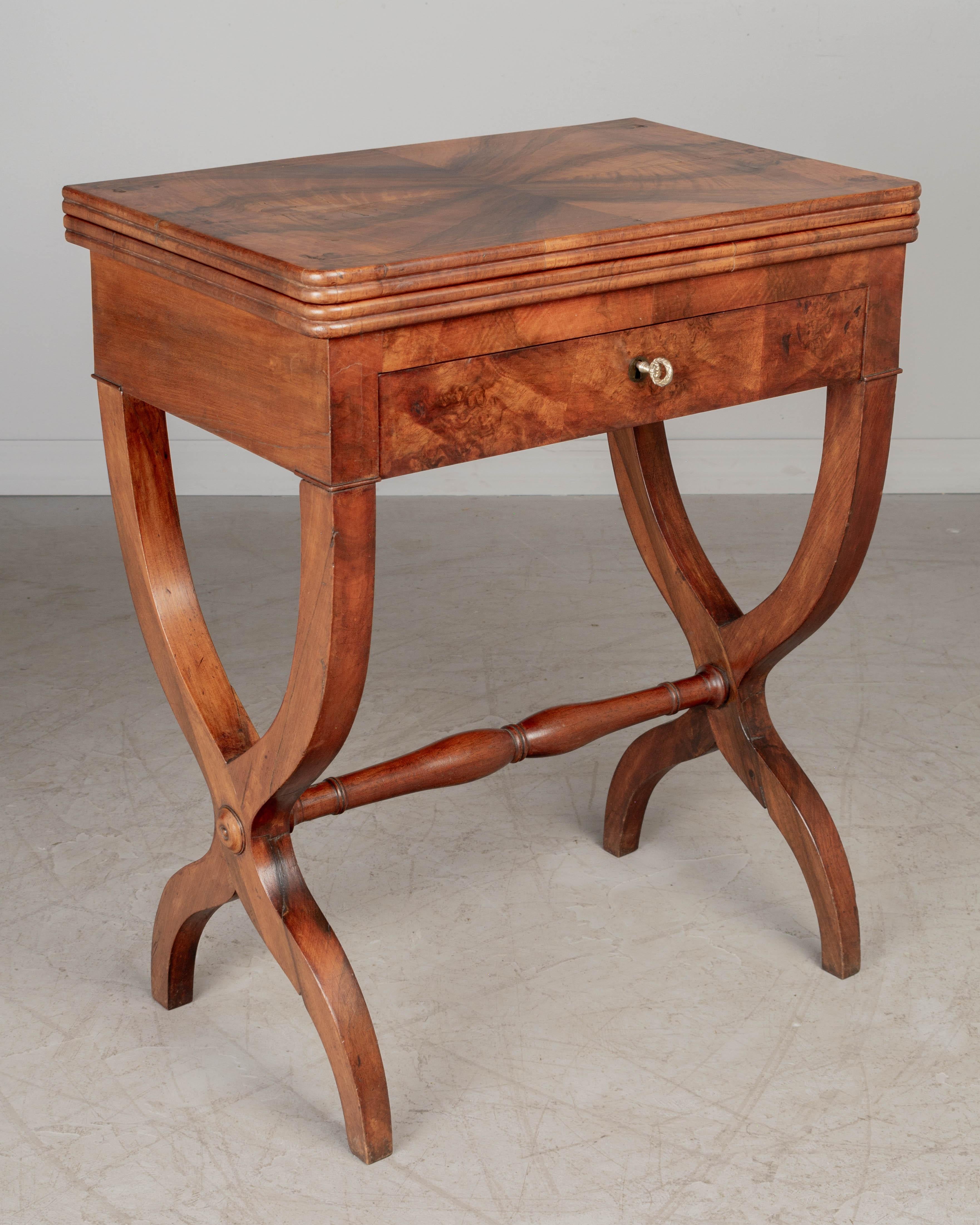 A 19th century French Charles X style flip top game table, or side table, with beautiful book matched veneers of walnut and mahogany. The top rotates and flips open to reveal a green felt covered surface and interior divided compartment for game