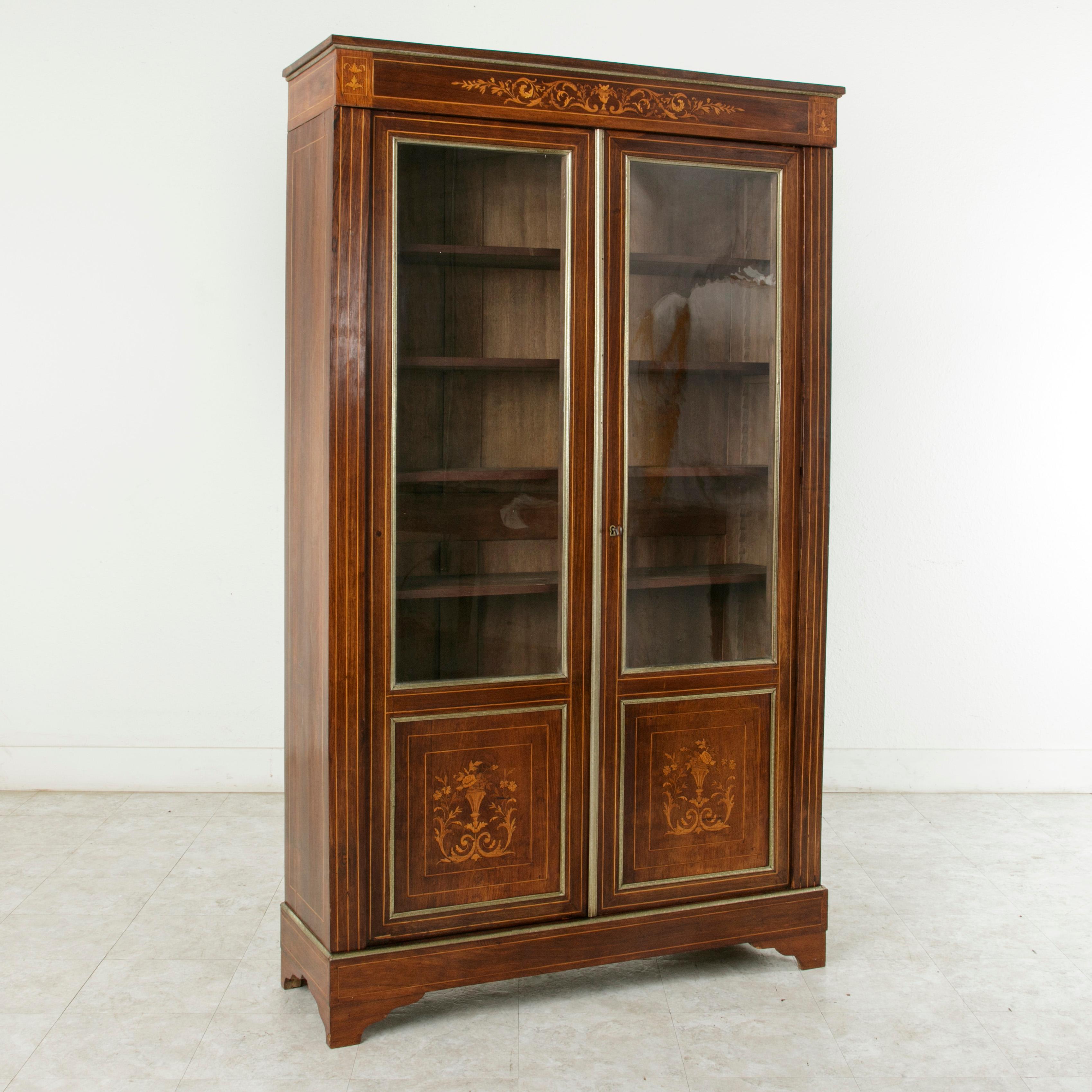 This early 19th century French Charles X period mahogany bibliotheque, bookcase, or vitrine features fine lines of lemon wood that frame the facade and make up the marquetry fluted columns. Unusual bronze banding decorated with a flower and leaf