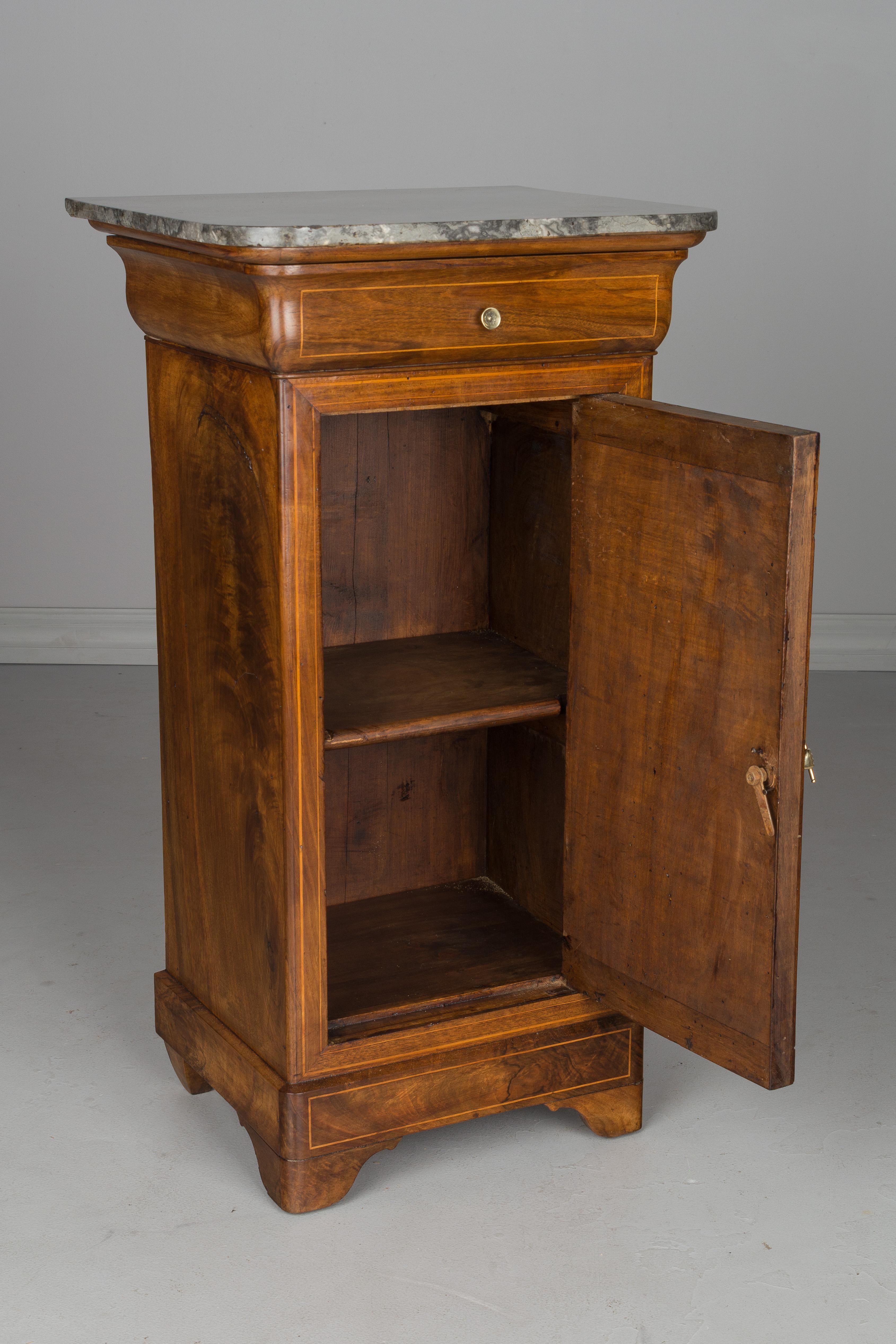 An early 19th century French Charles X side table or nightstand, made of walnut with fine inlay trim. Beautiful quality to the wood, the sides each with similar large knots. Waxed finish. Single dovetailed drawer with brass knob. Cabinet door with