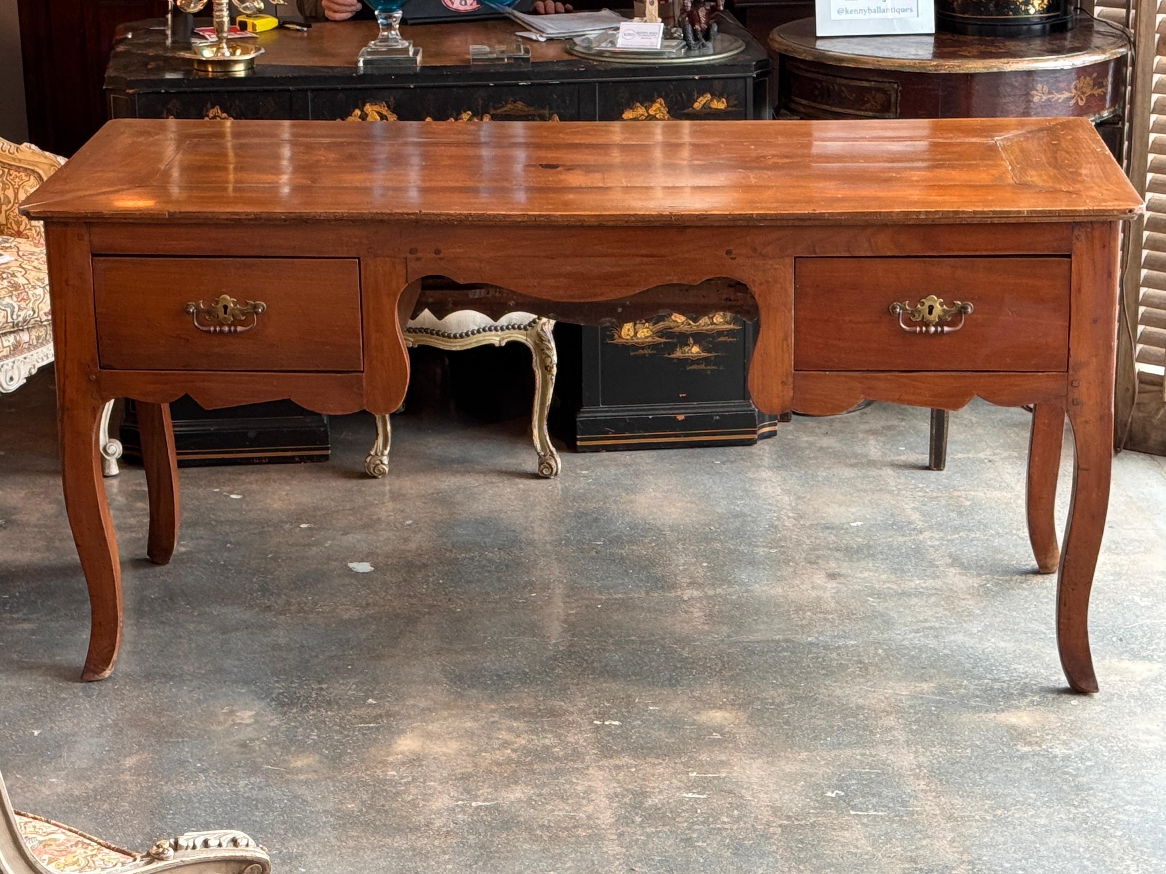 This French cherry desk features a thick plank top with breadboard ends, shaped apron, and two dovetailed drawers with later pulls. Cabriole legs and warm cherry grain give it a country provincial character. Old wear, surface marks, and age-use are