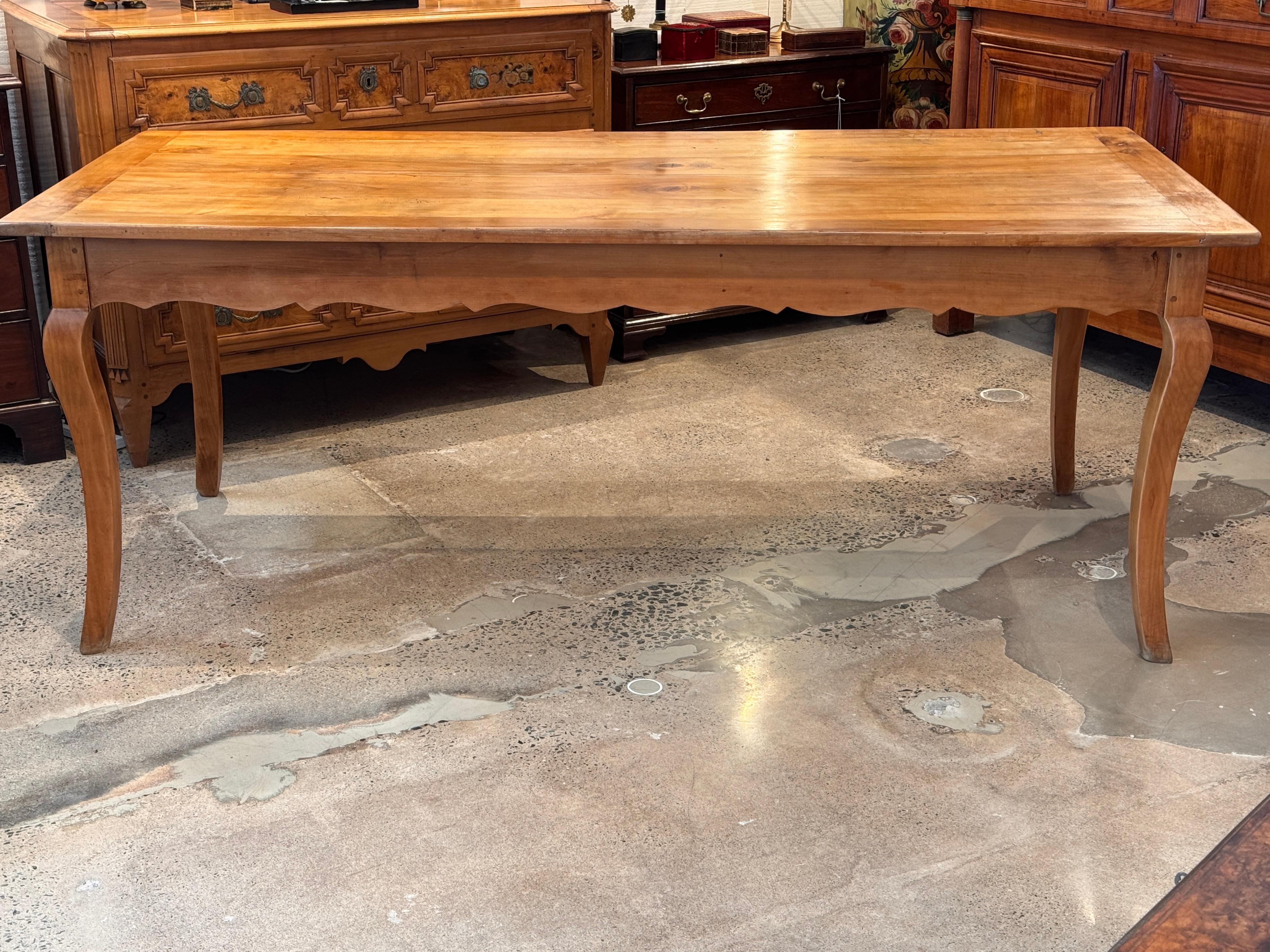 Table de ferme française du 19e siècle en cerisier à la patine chaude et mielleuse. La table présente un tablier festonné, des pieds en cabriole et un seul tiroir en bout de table. Les extrémités extractibles de la planche à pain prolongent la