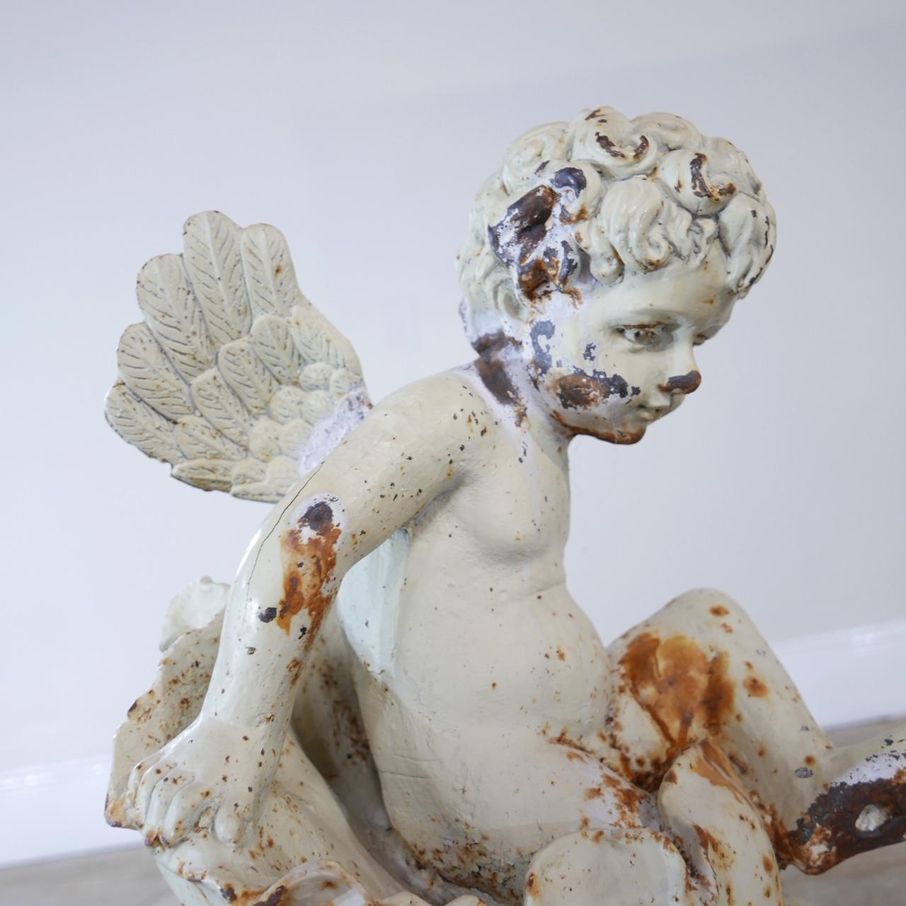 A garden feature in the form of a cherubic angel on a conch. 

Cast iron. 

French. 

Good condition generally considering its age, with a great patina.