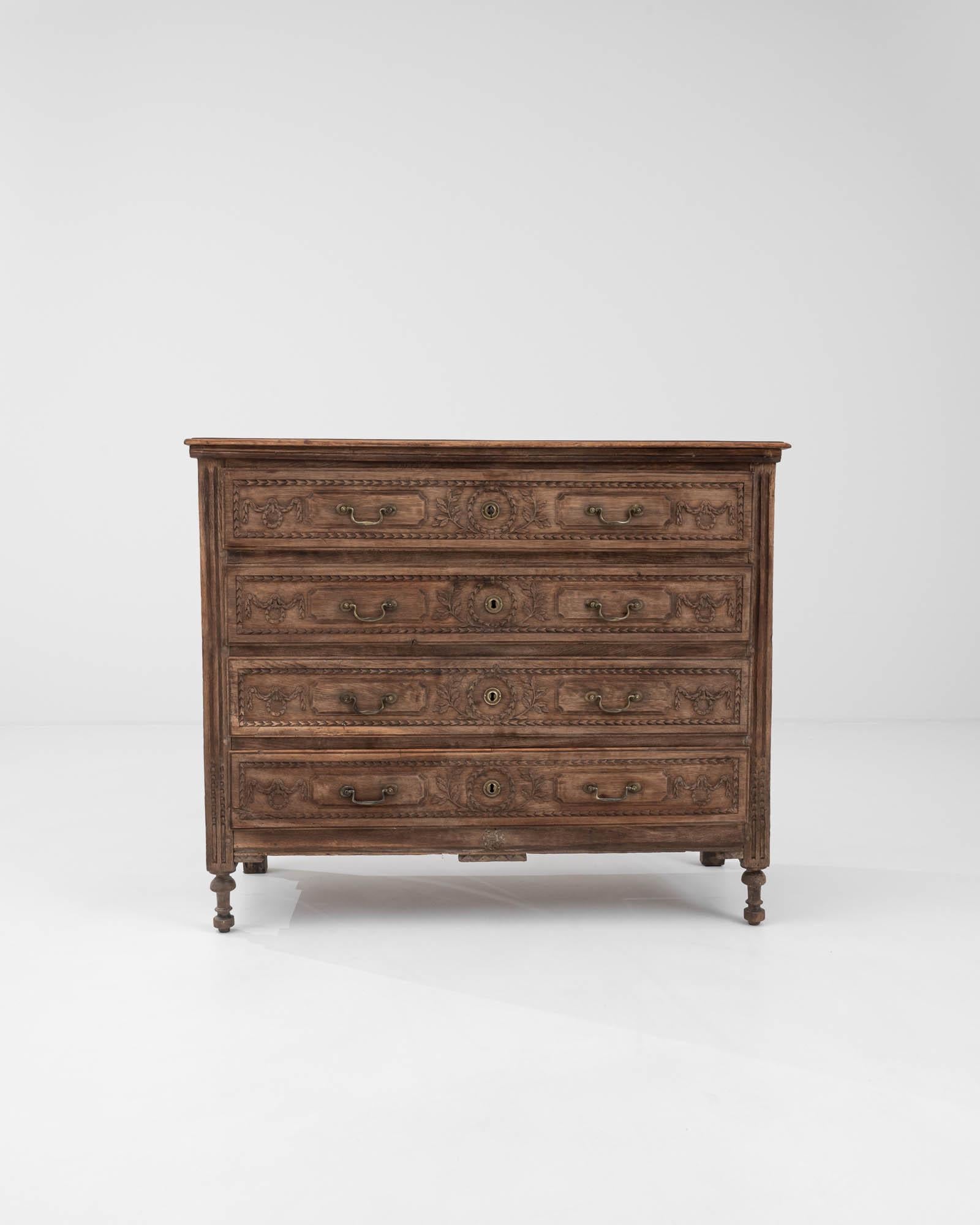 Artfully carved festoons and laurel wreaths embellish the four drawers of this 19th-century chest, crafted in France from refined wood. The richly adorned front harmoniously complements the meticulously carved geometric legs and elegant bail pulls,