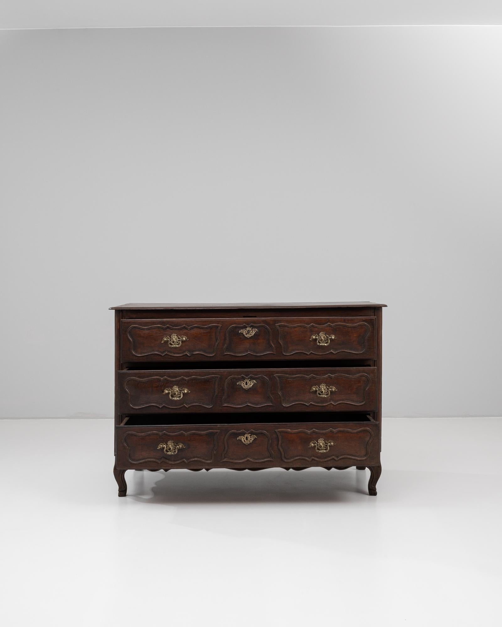 This 19th century French chest of drawers features a rich patinated finish that accentuates its elegant, curvaceous silhouette. Crafted in the Louis XV style, the piece boasts three spacious drawers adorned with shaped panel fronts and ornate brass