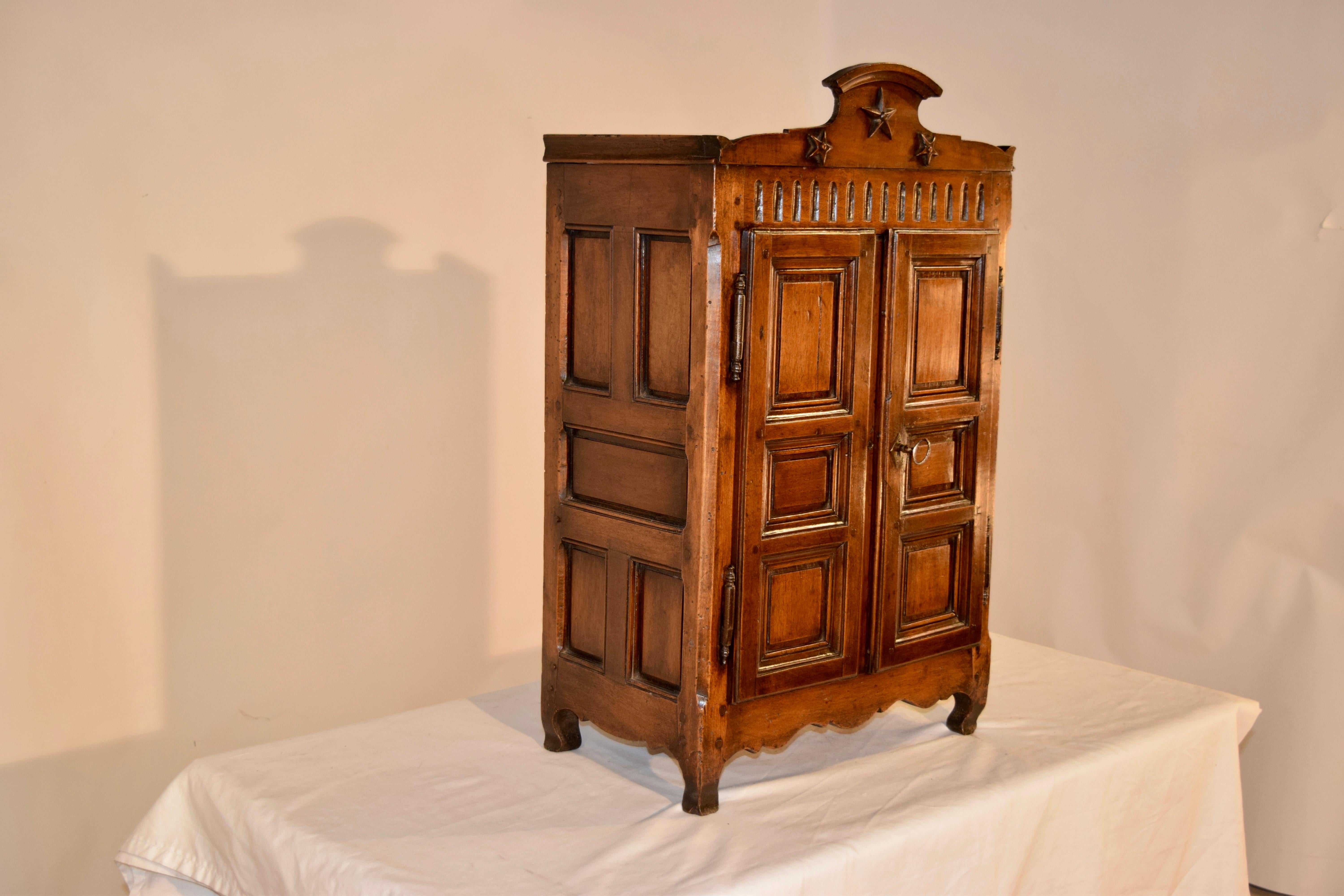 19th century chestnut miniature armoire from France. This is a wonderful piece of craftmanship, with a lovely crown following down to a case which is entirely raised panelled and pegged in construction. The doors open to reveal a finished interior