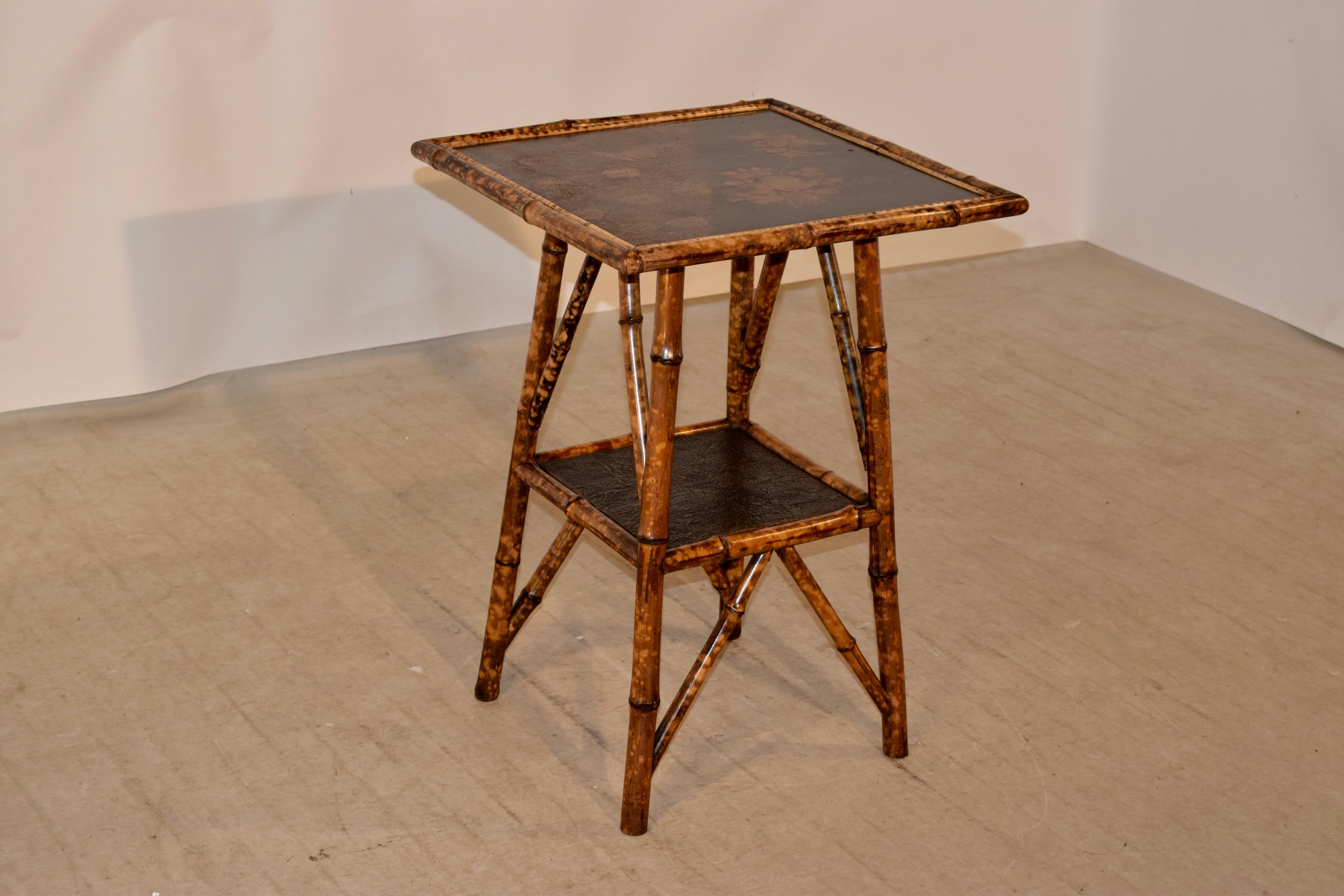19th century bamboo table from France with a hand painted chinoiserie top, following down to a lower shelf covered with hand painted paper. The table is made from tortoise bamboo and has splayed legs and stretchers.