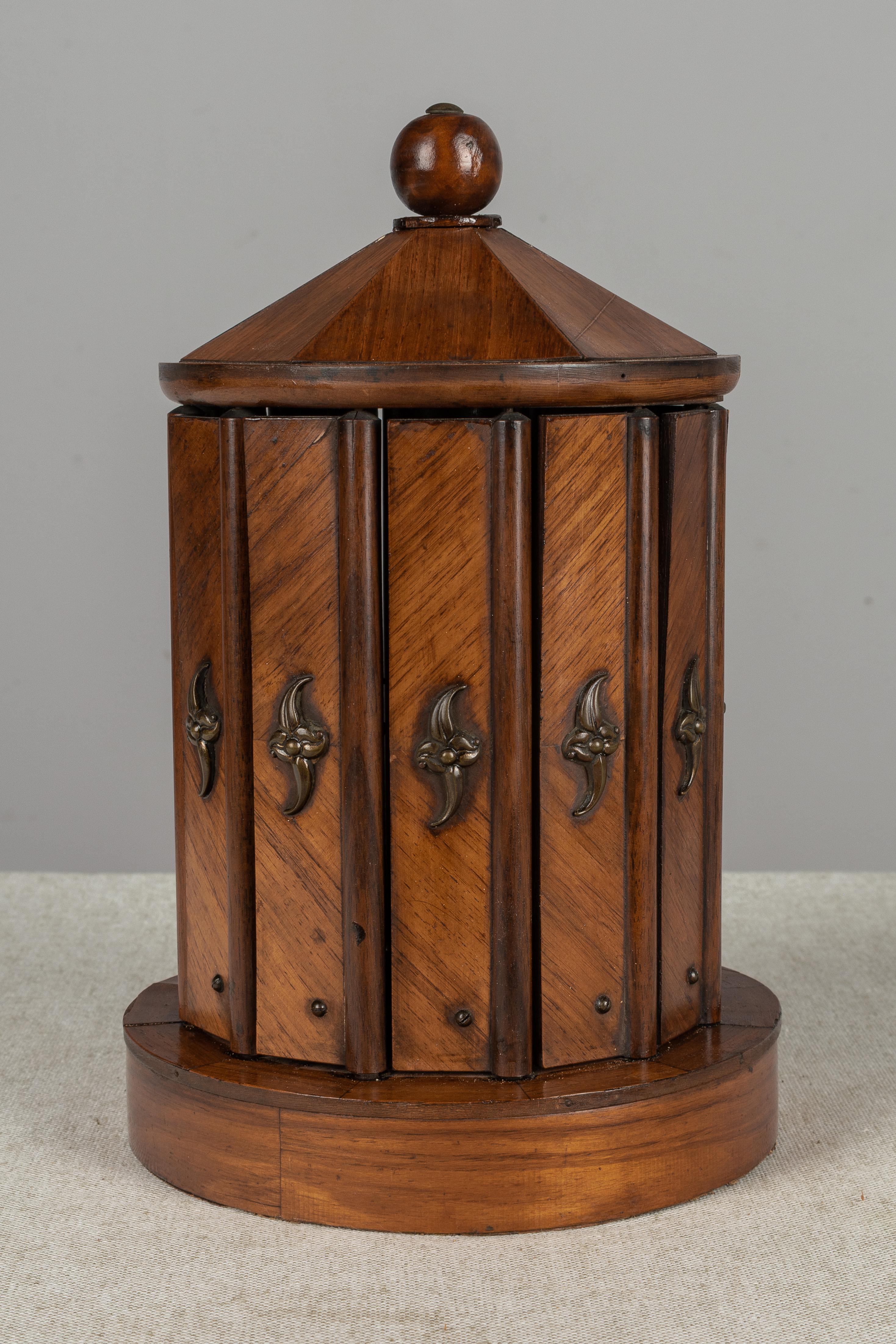 An unusual 19th century French circular cave à cigar, or cigar box, made of mahogany with decorative brass hardware. A clever mechanism, the louvered slats open by a turn of the knob at the top, revealing loops that hold twelve cigars. Fine