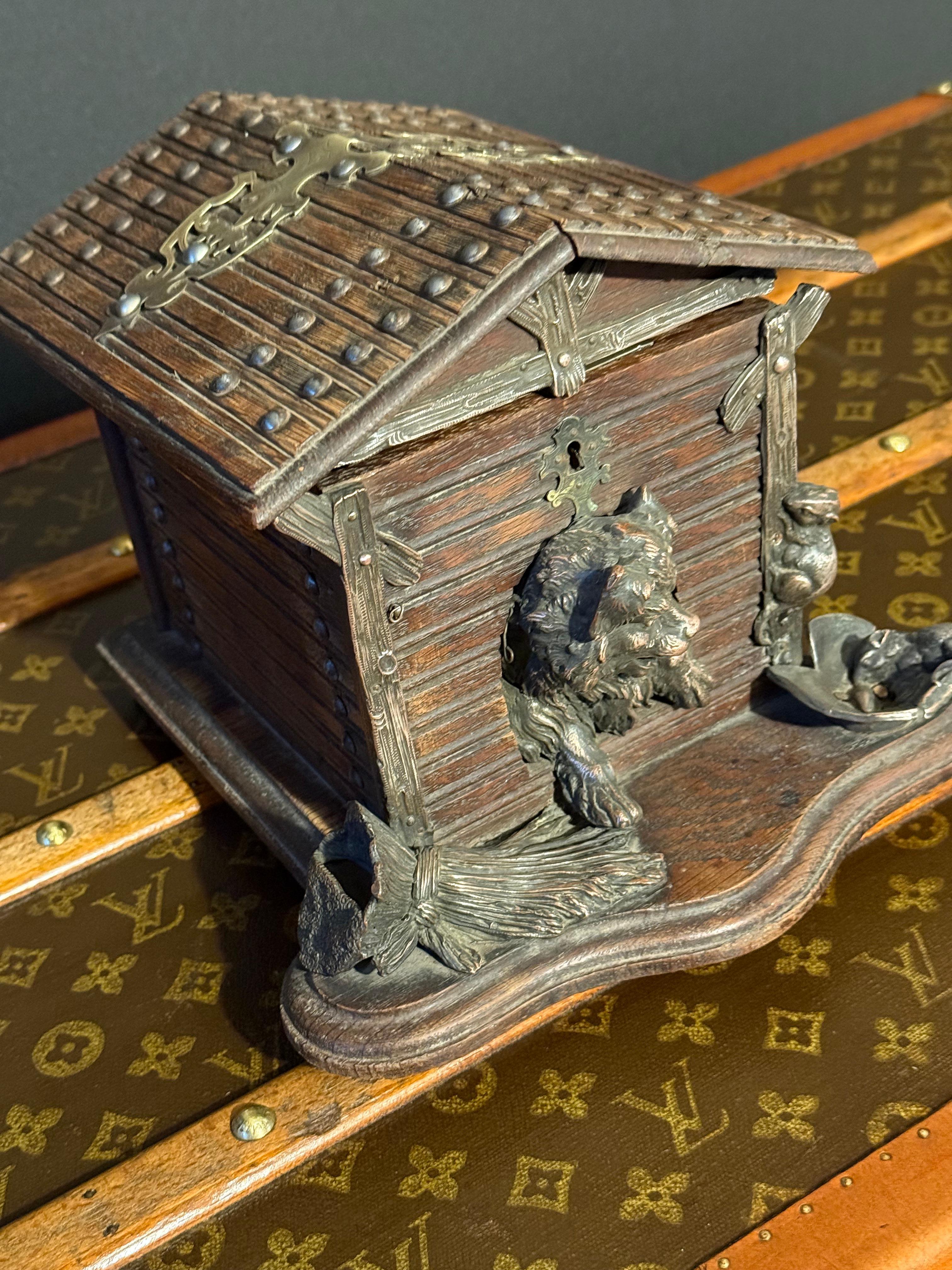 Esta caja para puros tiene la forma de un chalet rústico de madera, con una escultura detallada que imita tablones y vigas de madera. El techo, decorado con detalles metálicos, se eleva para revelar el compartimento interior. En la parte delantera,