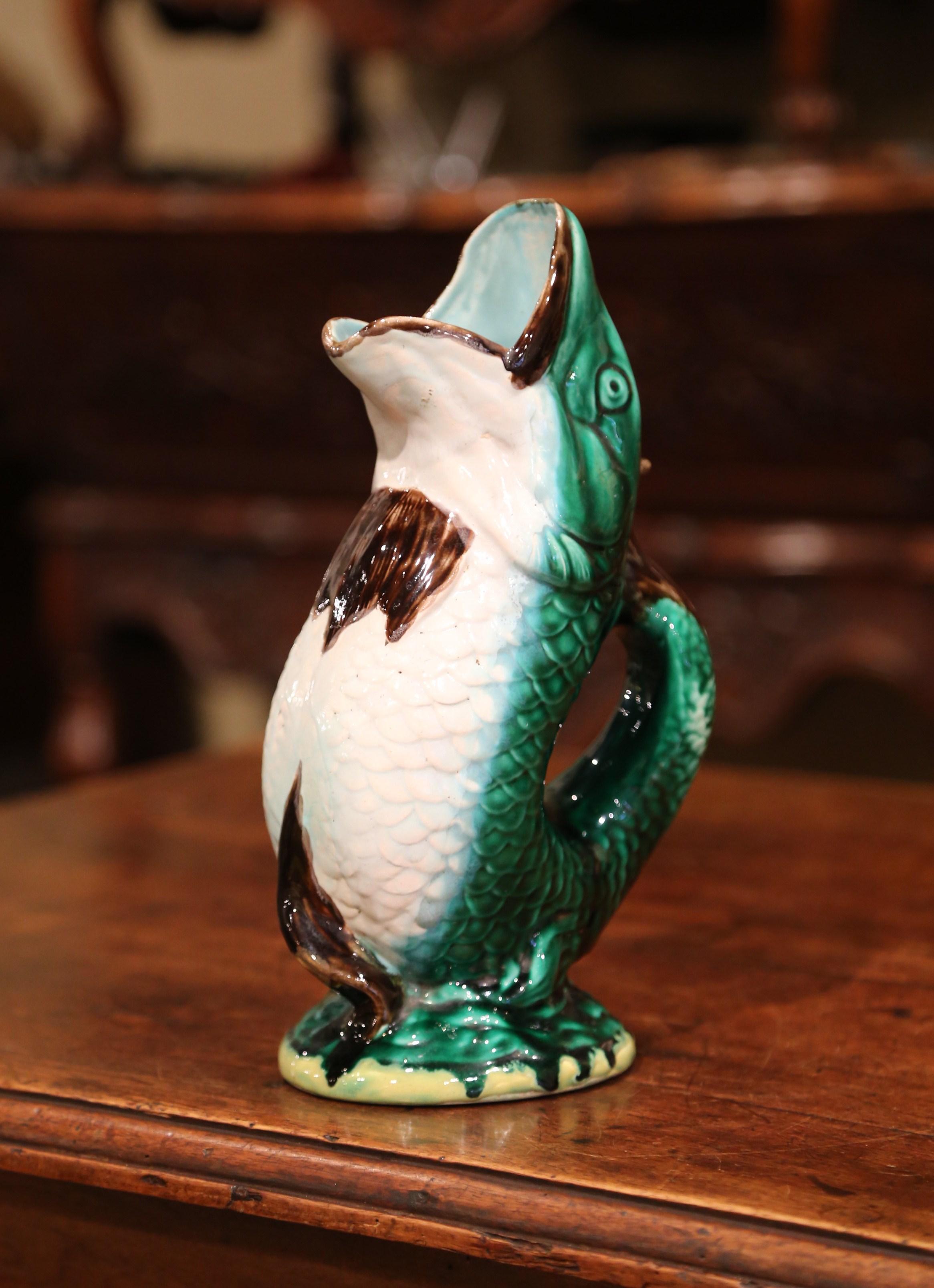 Aggiungi alla tua collezione di brocche questa colorata brocca antica in maiolica; scolpita a Clairefontaine, in Francia, intorno al 1890, la brocca in ceramica ha la forma di un pesce colorato in posizione eretta con la bocca spalancata. La brocca