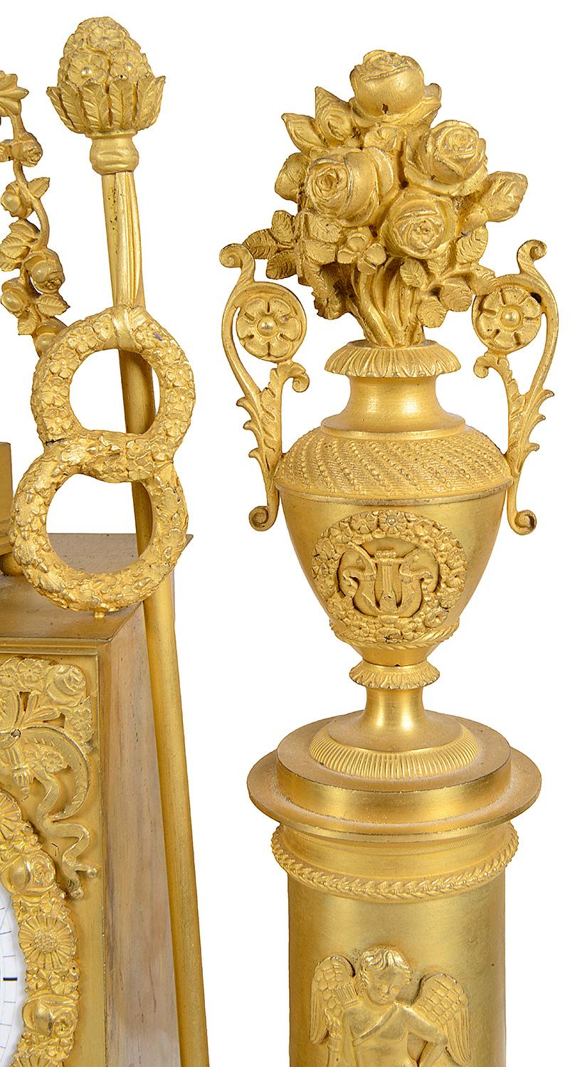 Agradable reloj de sobremesa francés de ormolina dorada de principios del siglo XIX, con una doncella clásica de pie frente a un espejo y un pedestal que sostiene un jarrón de flores. La esfera del reloj es de esmalte blanco con números romanos, un