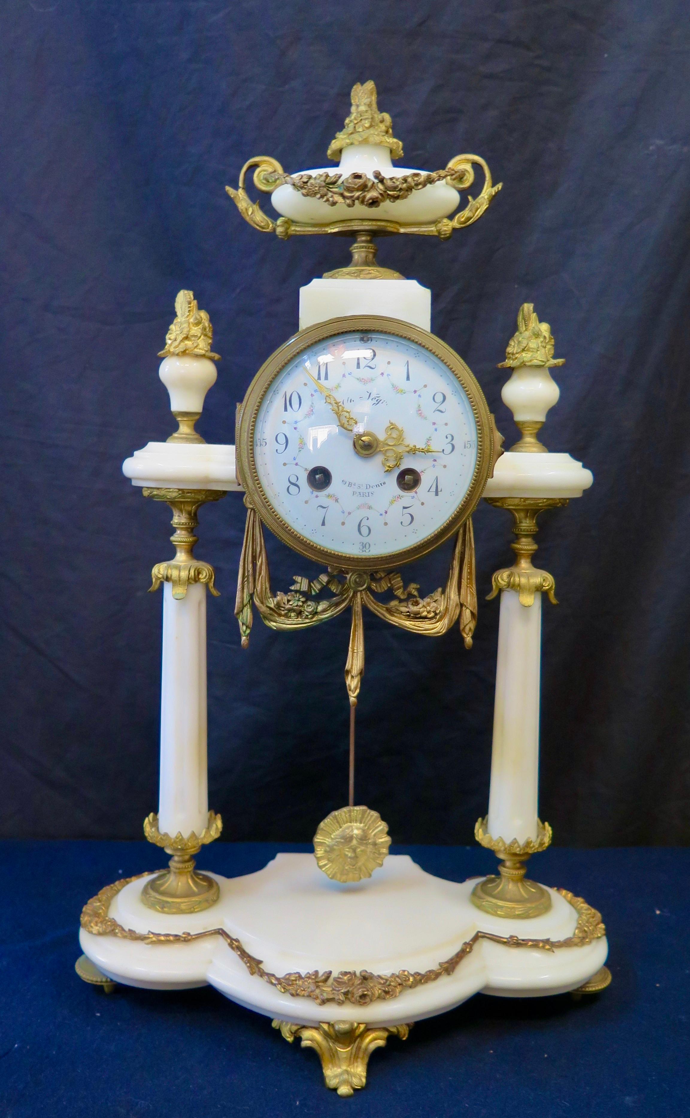 This vintage 19th century marble & dore' bronze clock set is beautifully designed in a Louis XVI motif. The clock features a decorative hand painted round enamel face with Arabic numerals, enclosed behind a hinged glass door. Clock works are within