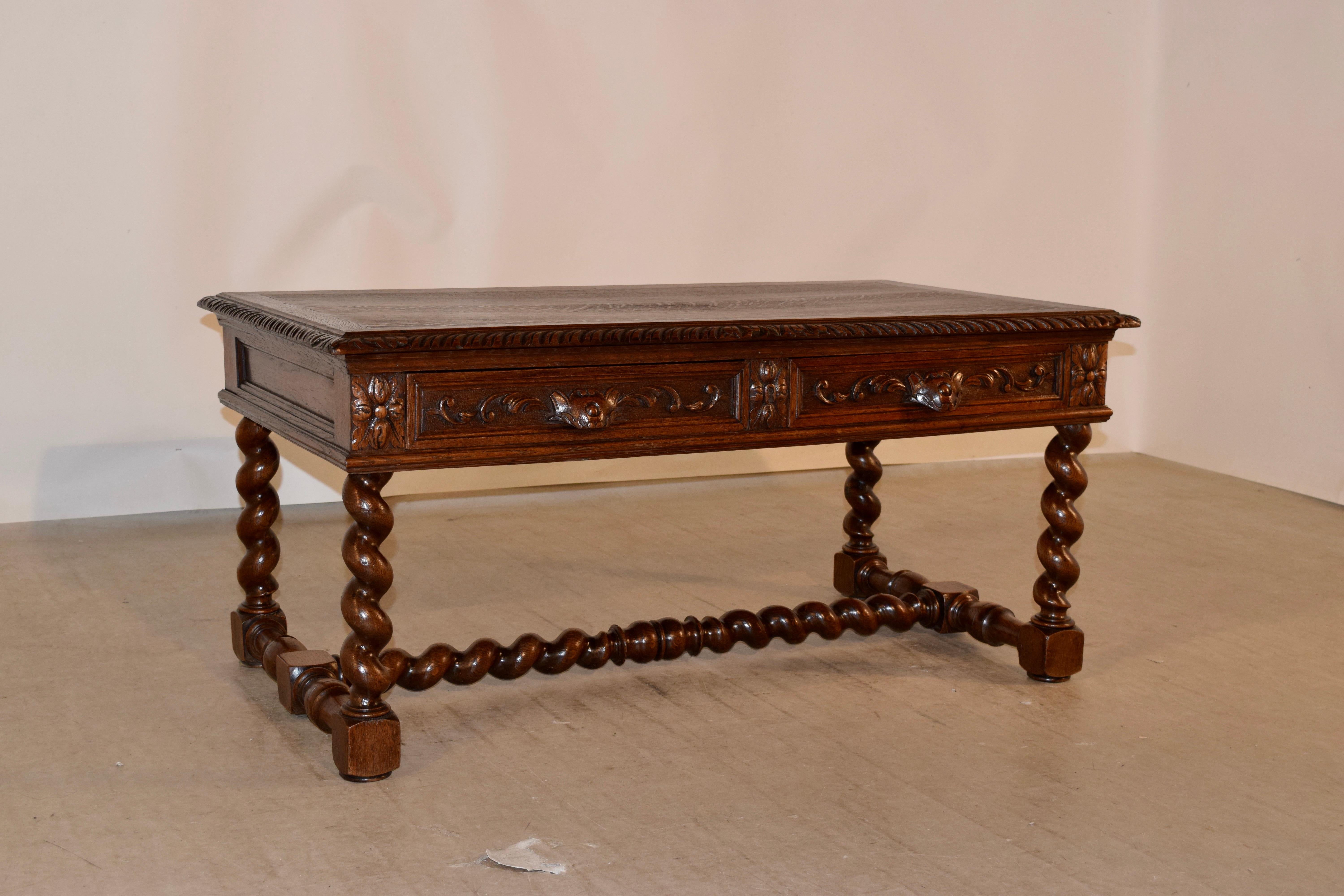 19th century coffee table from France made from oak. The top is banded around the edge and has a beveled and carved decorated edge as well. The apron is paneled and has two drawers with carved decoration in the front, over hand turned barley twist