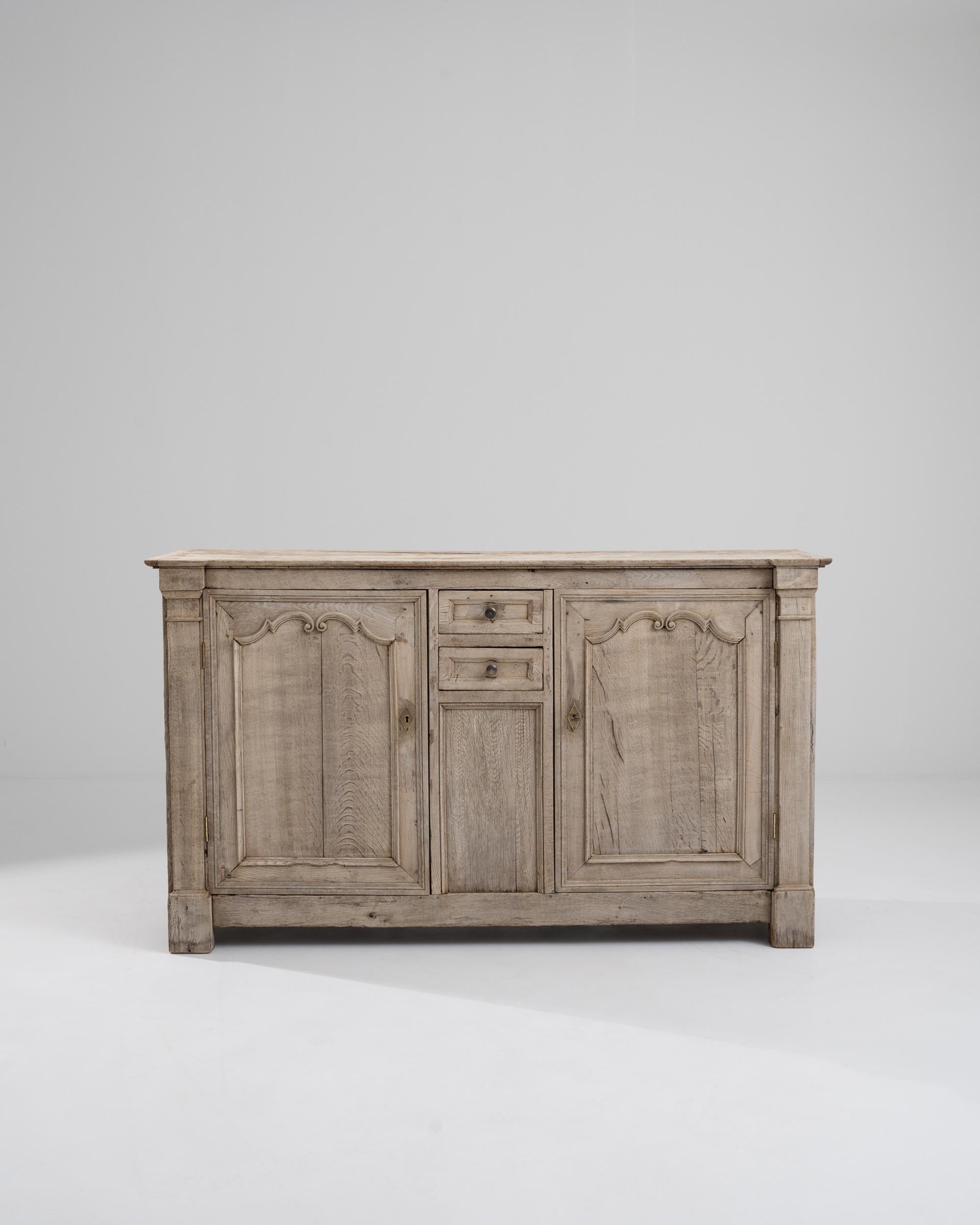 A wooden buffet from 19th century France. Spiraling panel details, careful joinery, and faux columns construct a buffet whose bleached oak shines almost like a chiseled marble block. This buffet offers ample storage as well, featuring four large