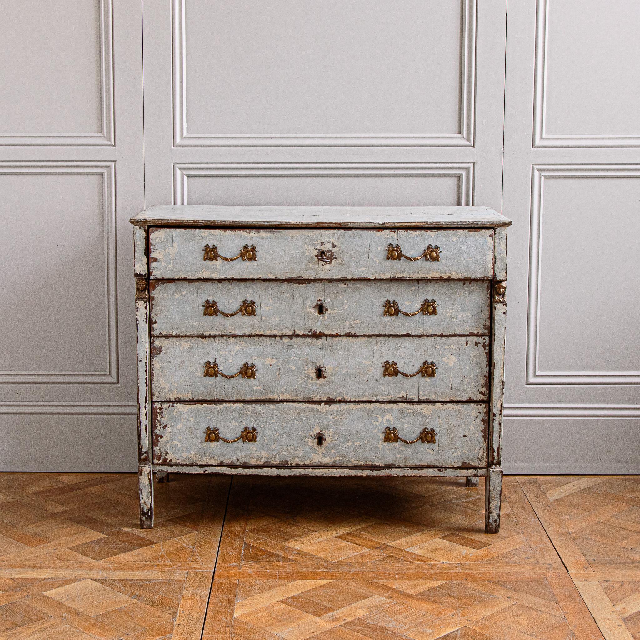 Un'antica cassettiera francese del periodo Impero, risalente al 1820 circa. 
Il corpo in legno massiccio è dipinto in un grigio/blu francese che presenta una patina interessante, strutturata e rovinata dall'età, che mostra parte della base dipinta a