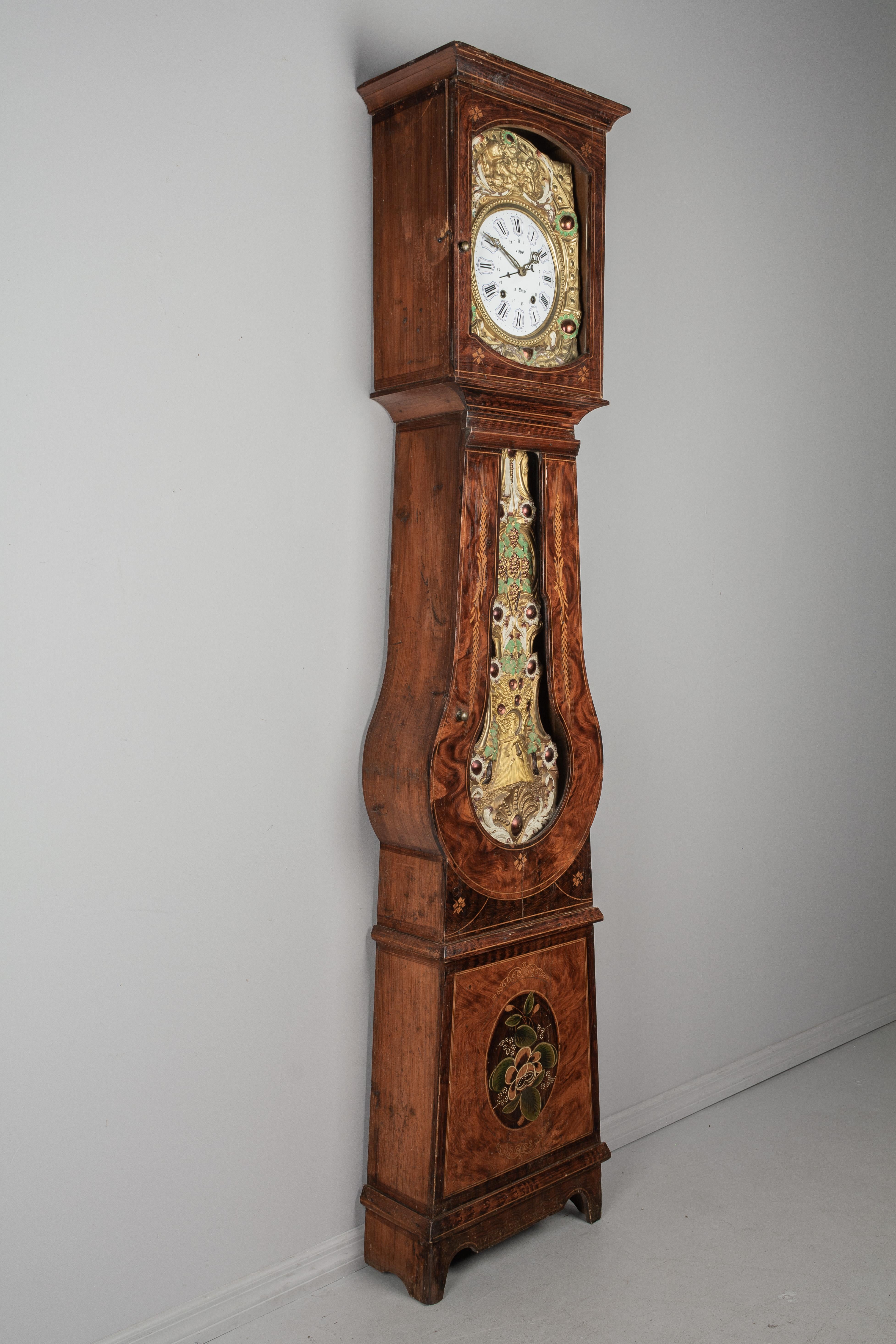 A 19th century country French comtoise, or grandfather clock, with polychrome painted pine case and embossed brass pendulum. Original seven day Morbier movement, professionally cleaned and in working order, having an enamel face signed by the