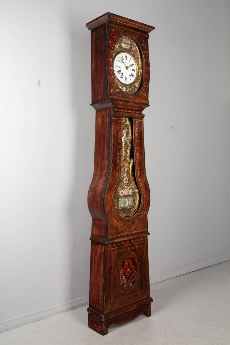 A French country comtoise or grandfather clock with polychrome painted pine case and embossed pendulum. Original seven day Morbier movement, cleaned and in working order, having an enamel face, signed by the clockmaker, Cadillon and the name of his