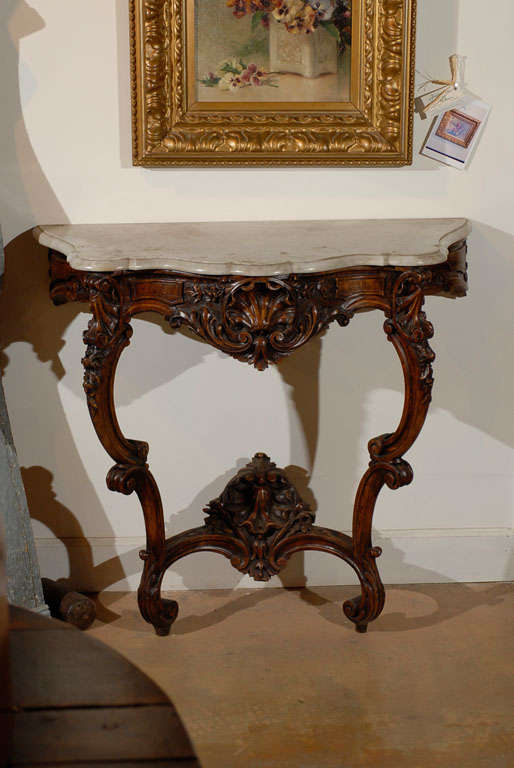 A French Rococo style carved wooden console table from the 19th century, with marble top, cabriole legs and cross stretcher. Born in France during the politically dynamic 19th century, this console table showcases the stylistic characteristics of