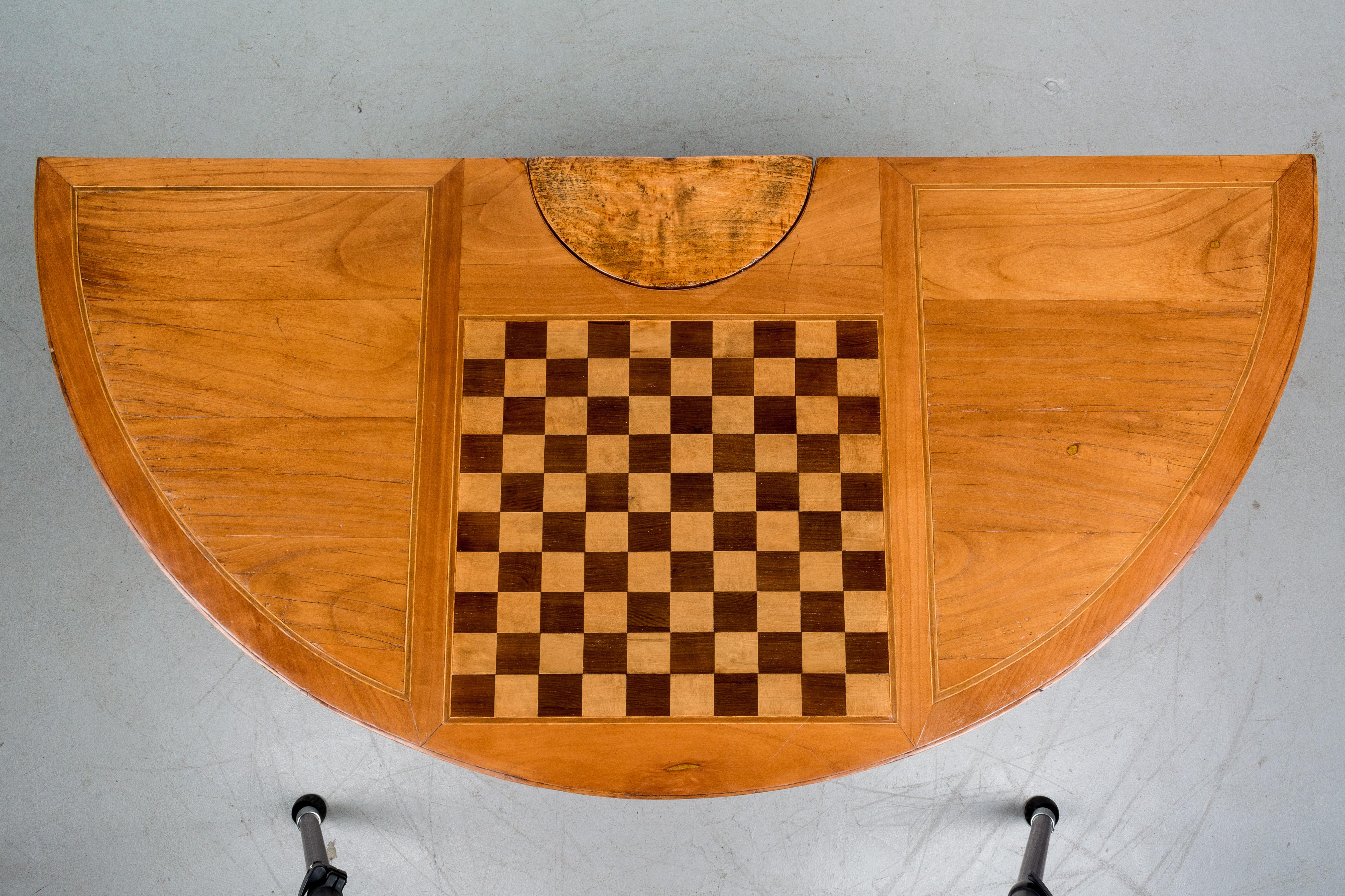 A 19th century French Louis XV style demilune flip top console game table made of solid cherry with a checkerboard made of inlaid veneer of cherry. The center leg pulls out to support the top and to reveal a drawer for storing playing pieces. The