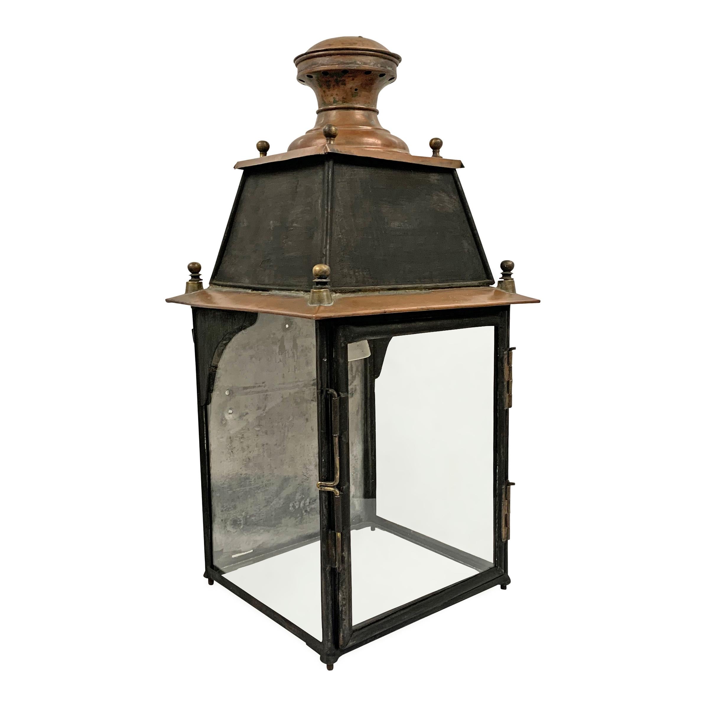 A charming 19th century French copper wall-mount lantern from a train station with a tall “mansard-style” roof with a round copper finial, and glass side panels, bottom, and door. Designed to be hung on a wall, but can also be used on a table.