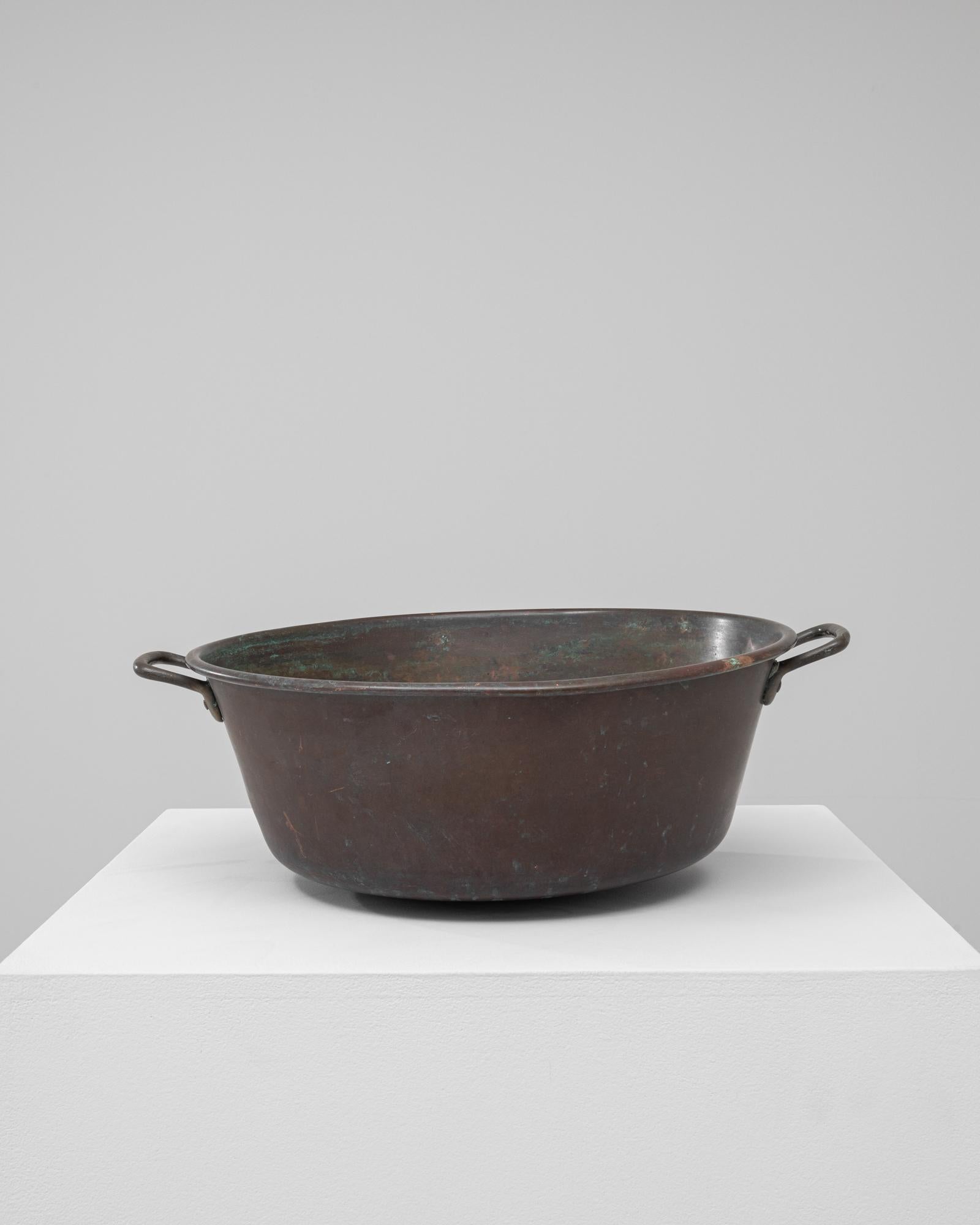 This 19th-century French copper pot is a fine example of traditional metal craftsmanship, valued for both its durability and aesthetic warmth. Hand-forged from solid copper, it features a deep, rounded basin with dual riveted handles designed for