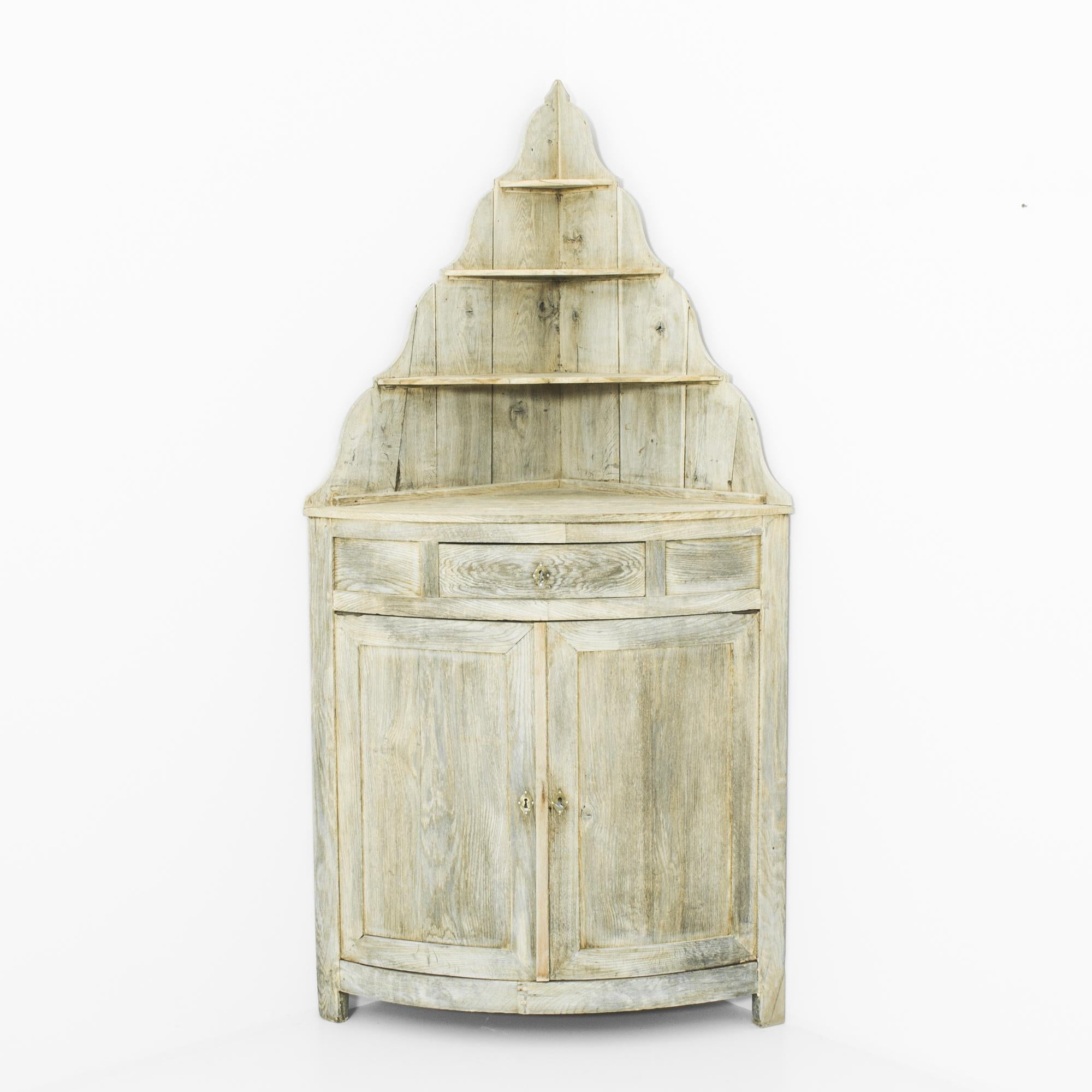 An oak corner cabinet from France, circa 1860. The unique silhouette creates a whimsical French Country aesthetic: the upper half ascends to a narrow point, like a turret or spire. The elegant contours of the upper shelves and the pale, alabaster