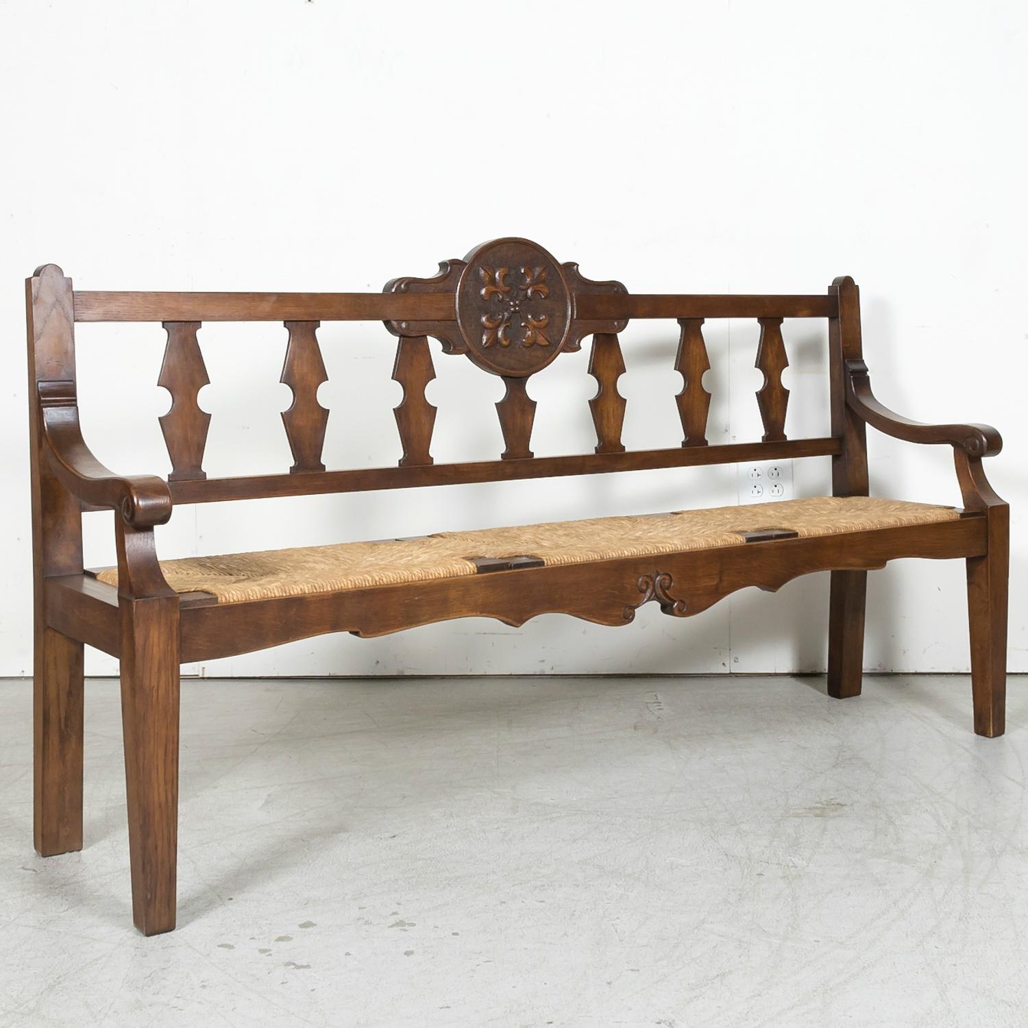 A 19th century French Country radassier or hall bench handcrafted of solid oak with a rush seat in Bayeux, one of the most beautiful medieval towns in Normandy, circa 1890s. This handsome antique bench seats three and features carved vertical slats