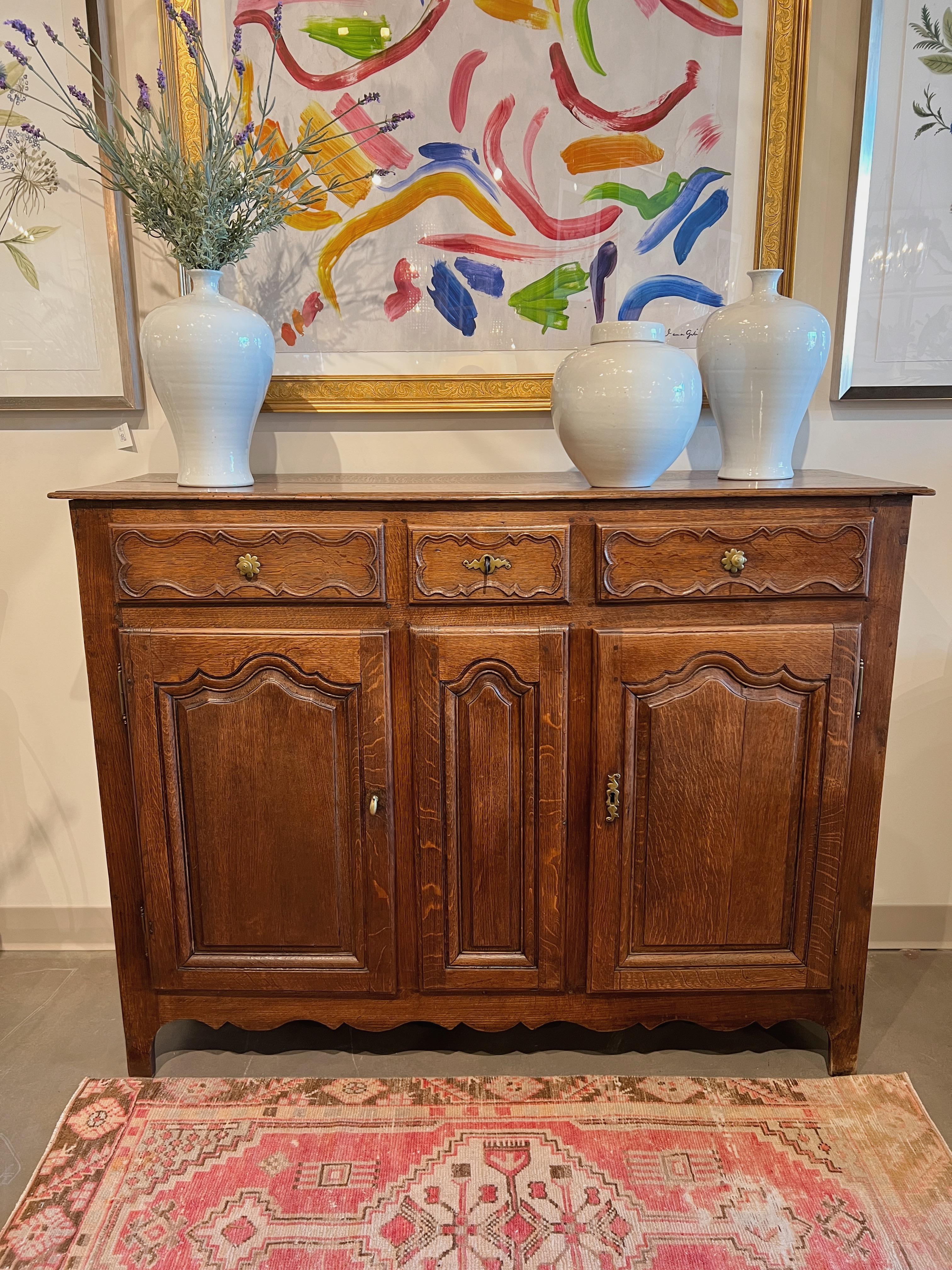 Circa mid 19th century France.

This handsome antique French buffet features a molded edge plank top above three drawers with beautiful carved faces. The outer drawers have floral brass knobs and the center drawer has a non-functioning lock & key.