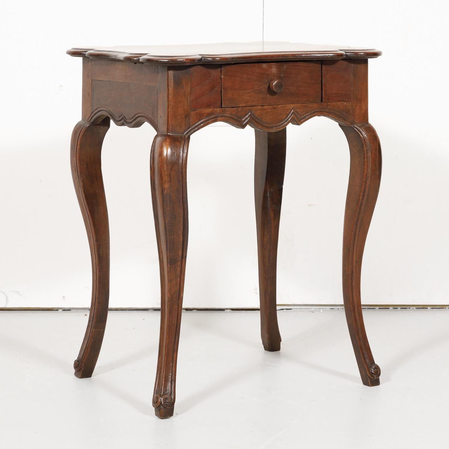 19th century French Country Louis XV style side table constructed of walnut in the South of France near Gordes having a moulded serpentine top that sits above a nicely scalloped apron with a single drawer. Raised on graceful cabriolet legs ending in