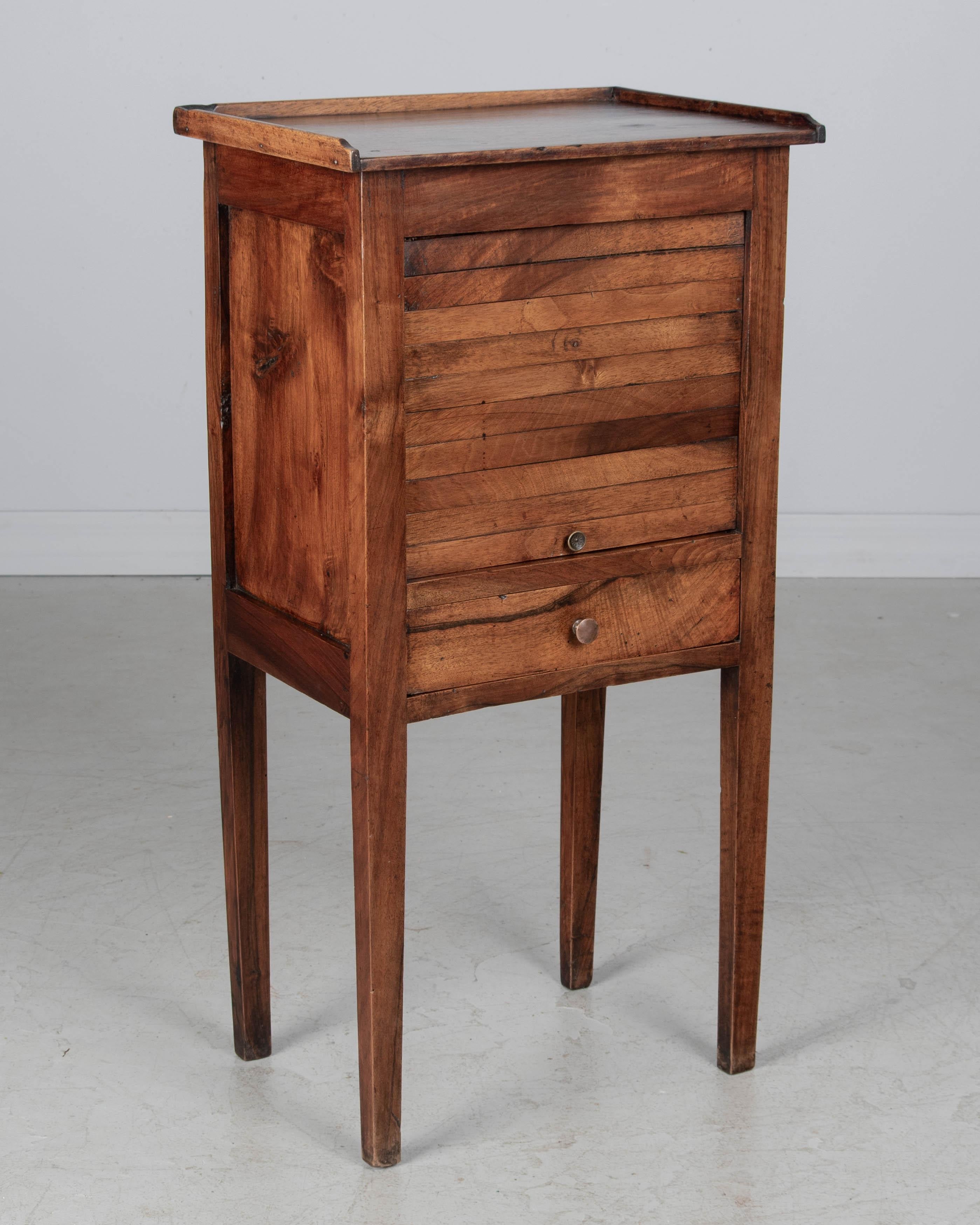 Table d'appoint, ou table de nuit, en noyer du XIXe siècle, de style français, avec une porte à tambour verticale au-dessus d'un tiroir à queue d'aronde. Finition sur les quatre côtés. Petits boutons en laiton. Un pied est plié, mais la table est