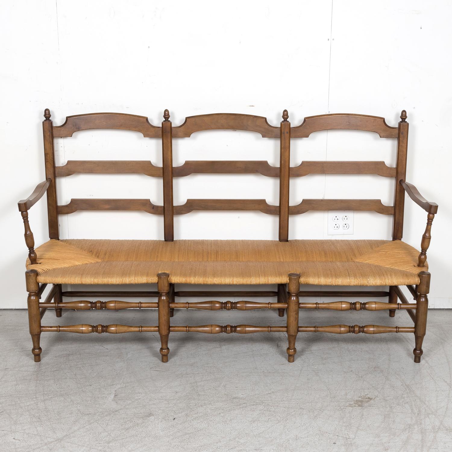 A 19th century French Country ladder back radassier or settee handcrafted in walnut, circa 1890s. This double arm Provençal bench seats three and features a handwoven rush seat and ladder-back. Raised on turned legs with stretchers. A wonderful,