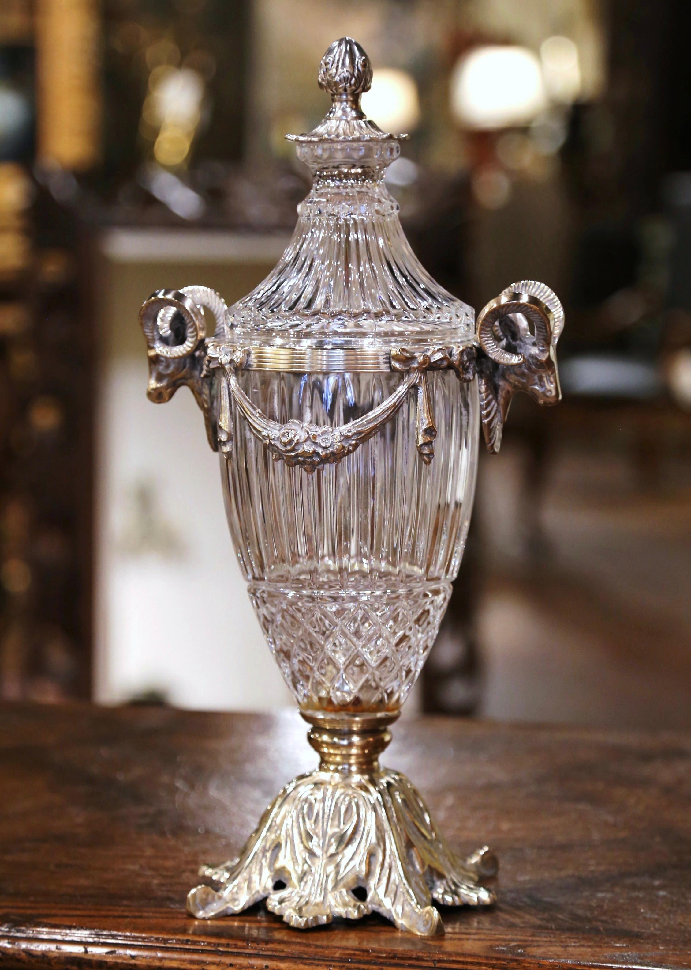 Created in France circa 1880, the elegant antique vessel with lid is made of cut crystal decorated with silvered bronze mounts; the tapered vase stands on a wide base decorated with acanthus leaf motifs. The top features two ram heads figures