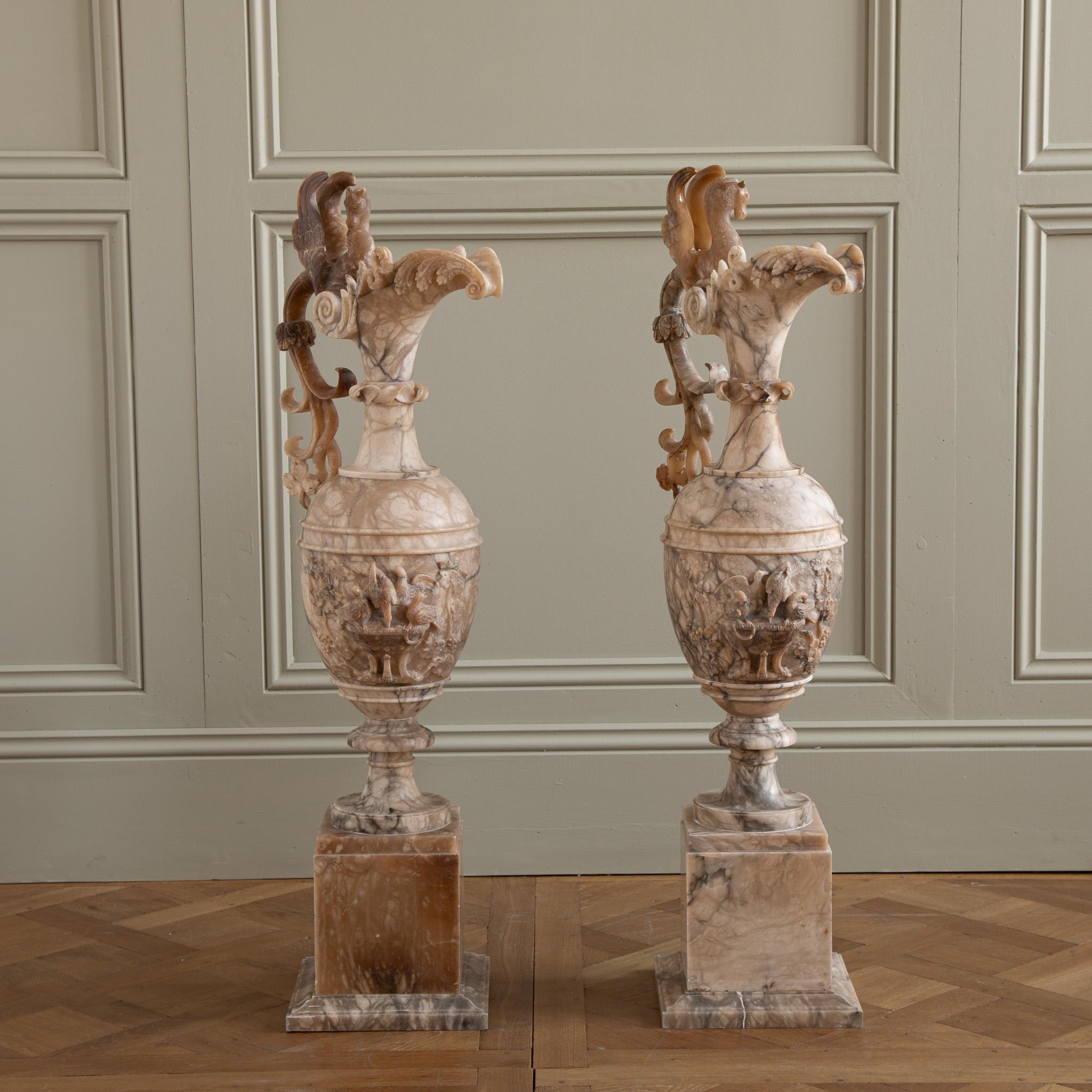 An exceptional pair of elegantly tall, 19th Century, French Decorative pitchers on plinths, hand carved in a beautifully veined Alabaster marble. The Neo Classical style pieces, each feature a hippocampus, the winged sea horse of Greek mythology