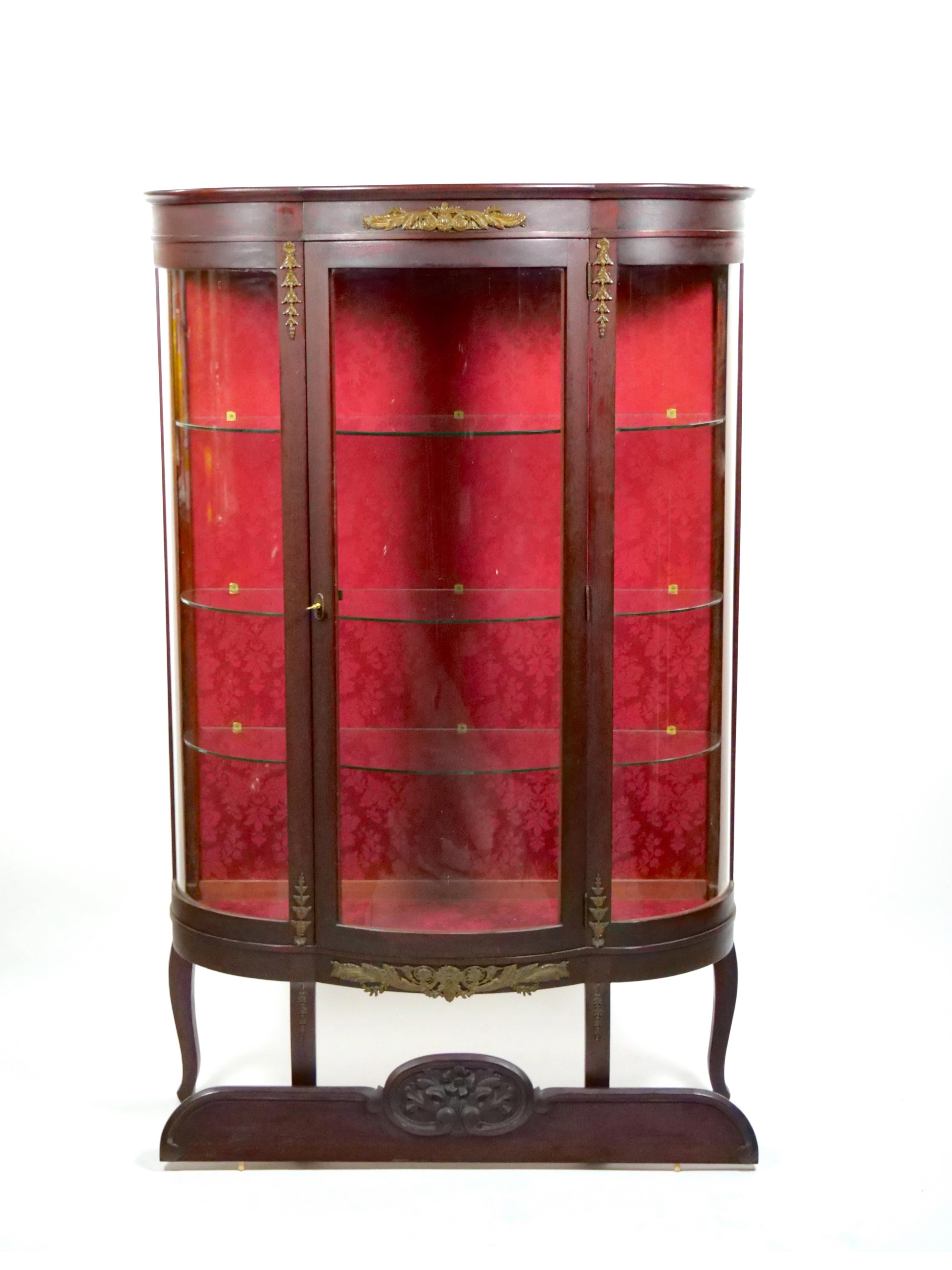 
Embrace the timeless allure of our antique demilune-shaped vitrine and china cabinet, Beautifully finished in a warm, inviting red stain. This exquisite piece showcases an array of intricate details, from the graceful foliate motifs to the ornate