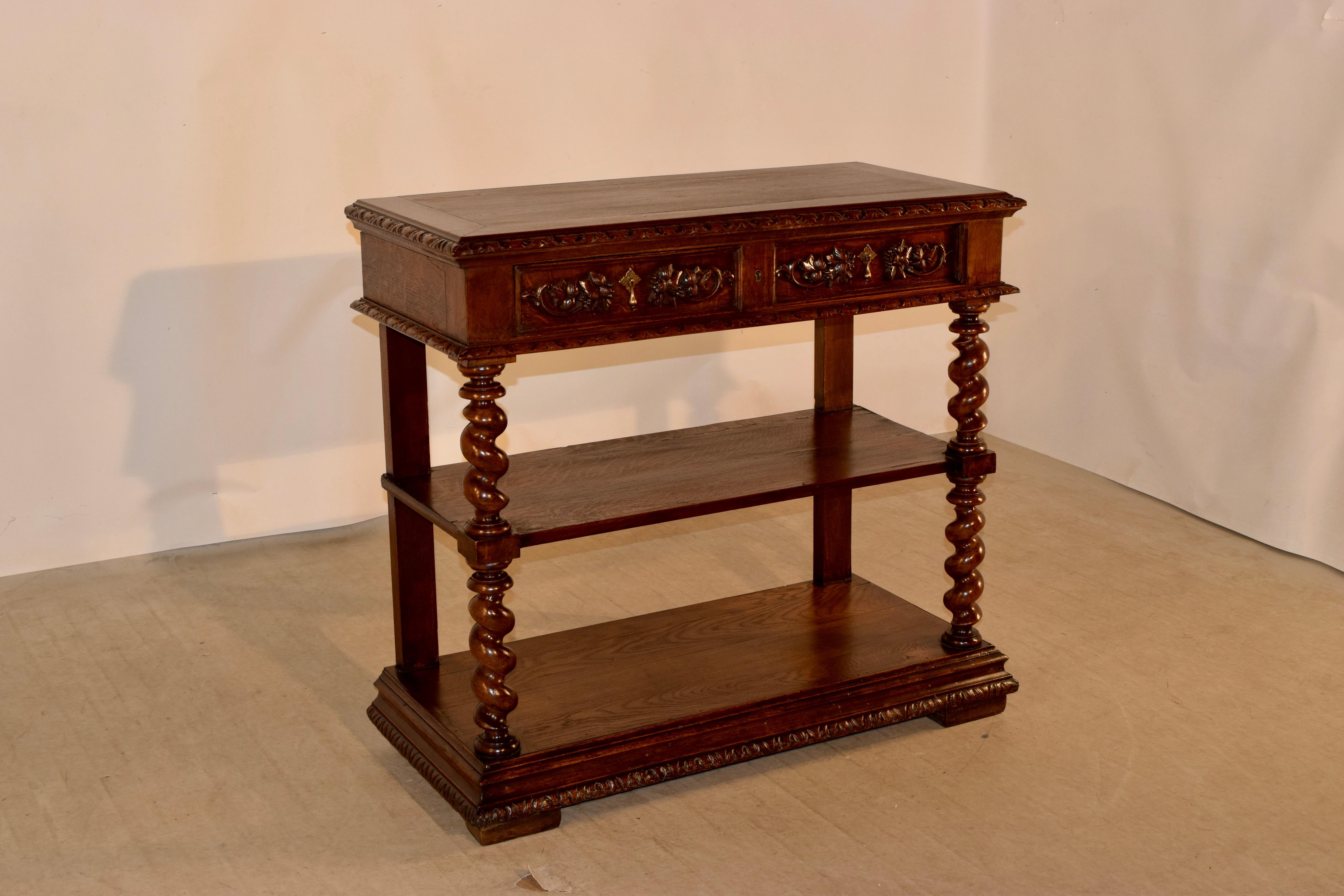 19th century French dessert buffet made from oak with a banded top which has a beveled and carved decorated edge, following down to two drawers, both with molded edges and hand carved decorations. The piece has two shelves, separated by hand turned