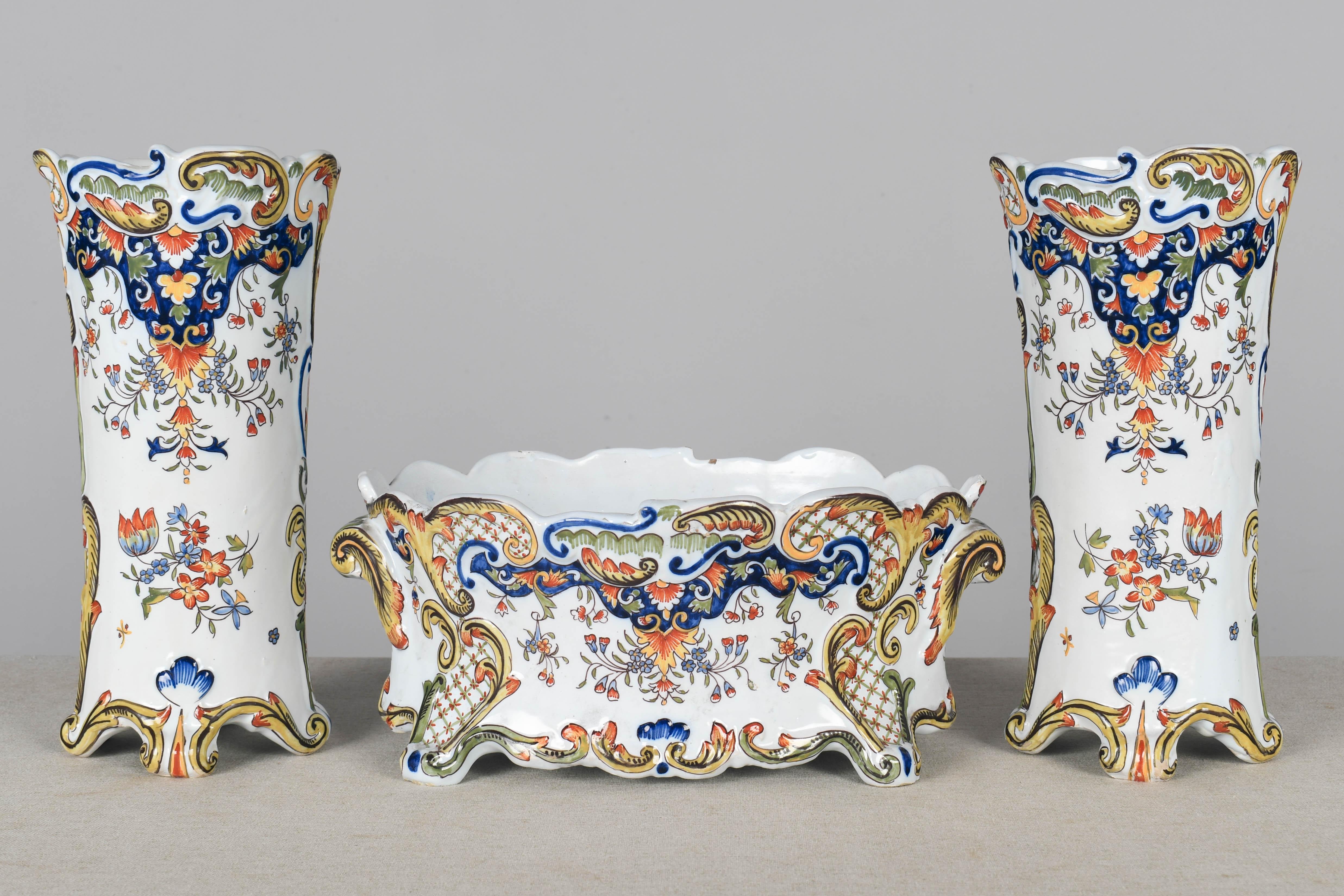 Una parure di tre pezzi in maiolica francese Desvres del XIX secolo che comprende una jardinière, o fioriera, e due vasi. Dipinto a mano con un tipico disegno floreale con bellissimi colori vivaci di blu, verde, giallo e rosso su fondo bianco. La