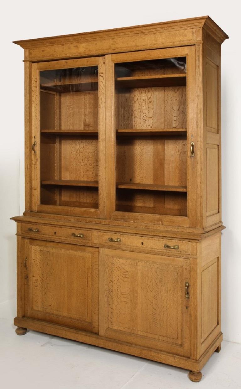 19th century French Directoire bleached oak bookcase with two drawers and brass hardware. Sliding glass doors on the upper shelving, sliding wood doors on the lower cabinet. Shelves are adjustable. Bun feet. 

Measures: Upper interior depth: